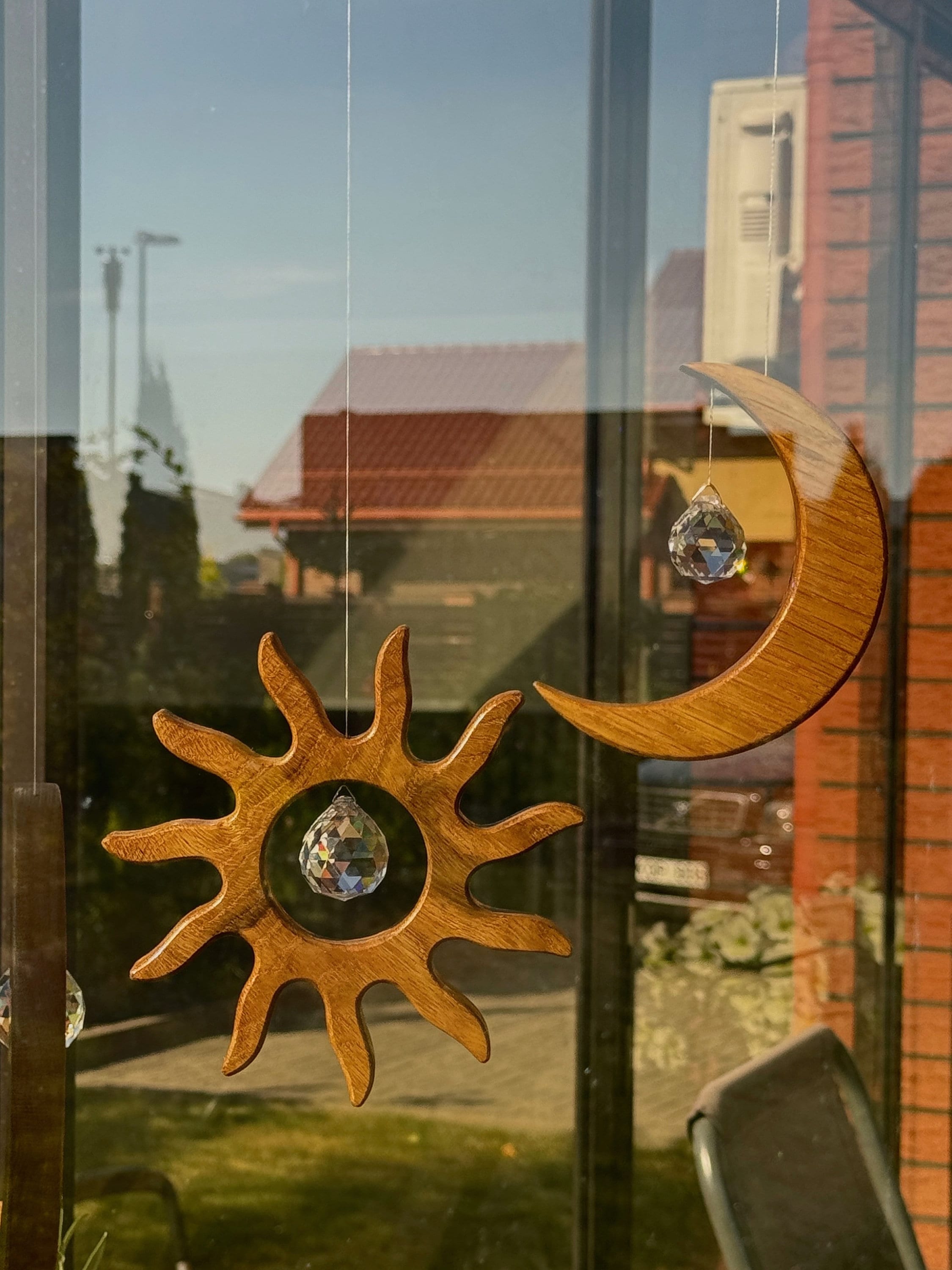 Handgefertigter Sonnenfänger aus Eichenholz (Oak) in Sonnenform with a central Asfour crystal prism. The Solstice wooden suncatcher casting rainbows on a white wall. Hochwertige Wohndekoration und Regenbogenmacher für Fenster oder Balkon.