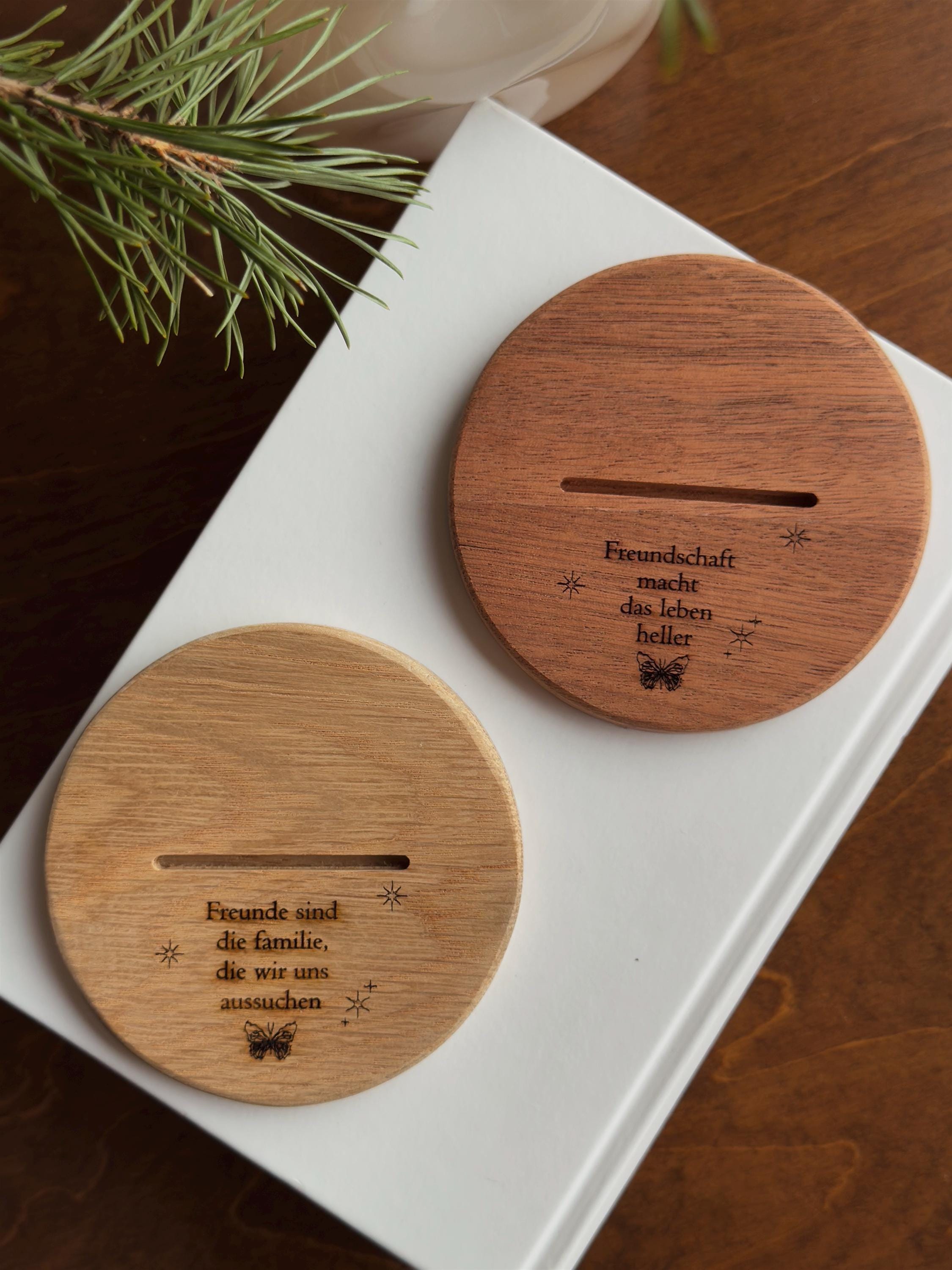 Two wooden coasters with engraved text on a white surface with a branch in the background.