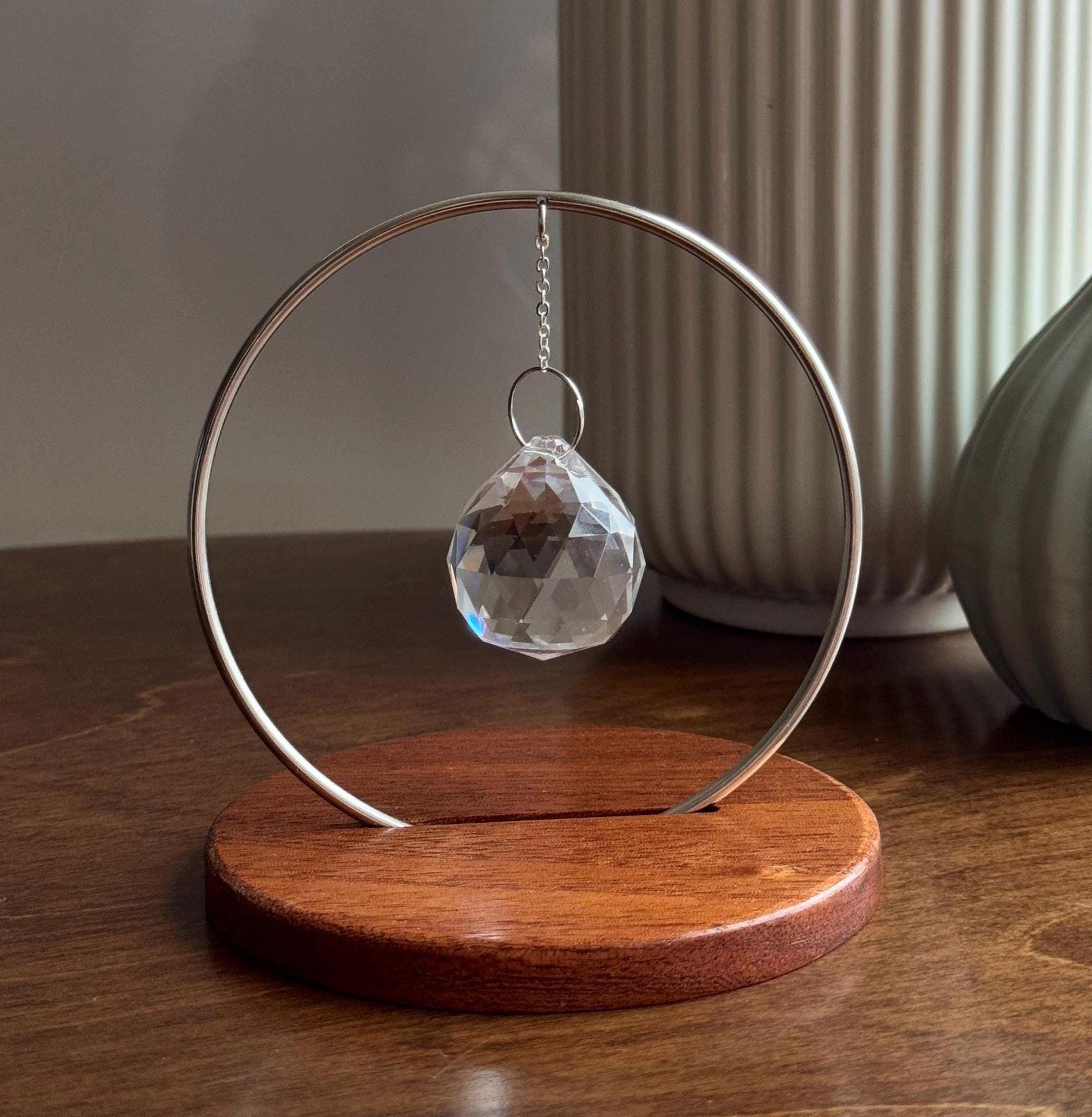 The Circle tabletop suncatcher featuring a silver stainless steel ring and faceted crystal prism casting vibrant rainbows on a white surface.