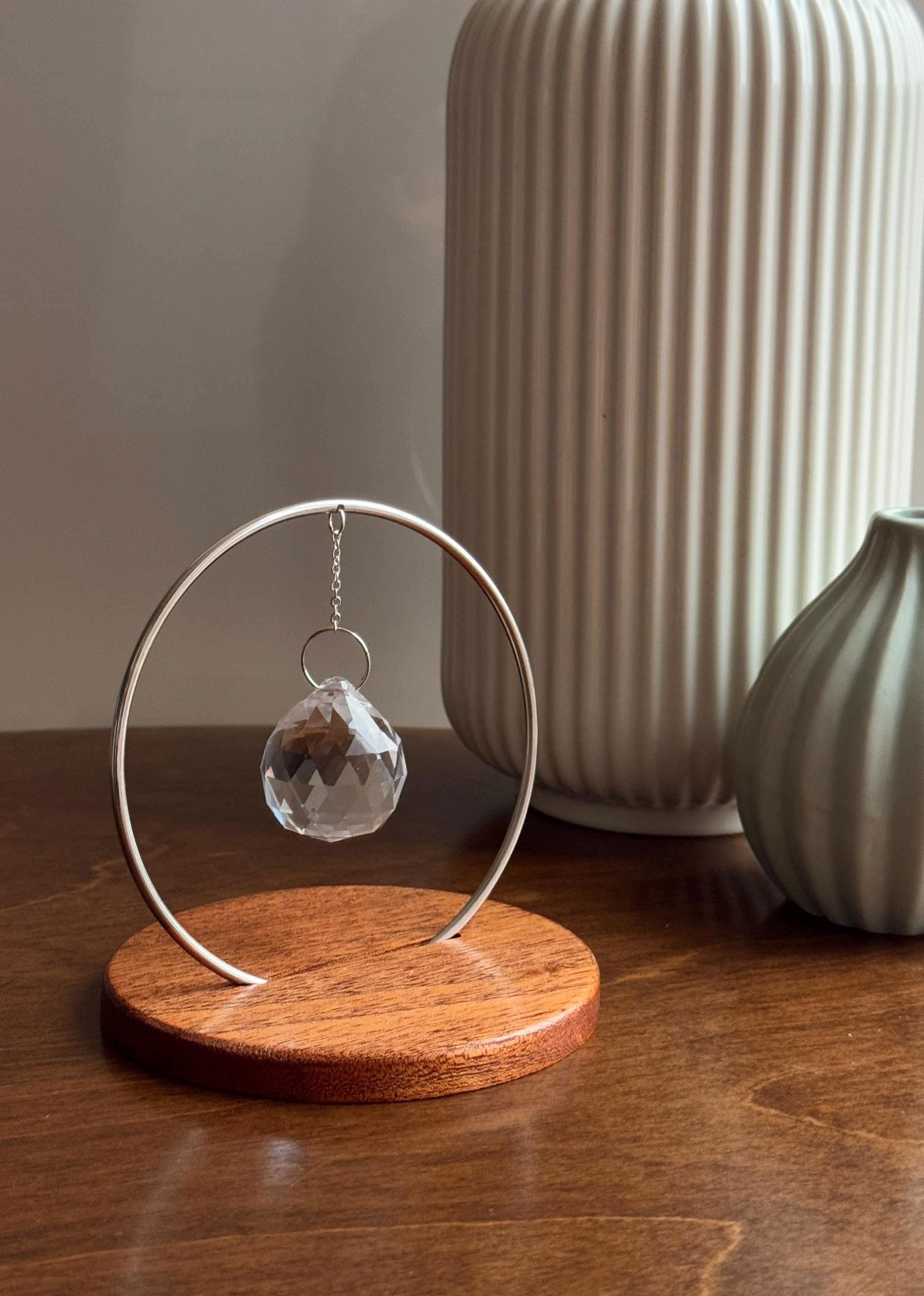 The Circle tabletop suncatcher featuring a silver stainless steel ring and faceted crystal prism casting vibrant rainbows on a white surface.