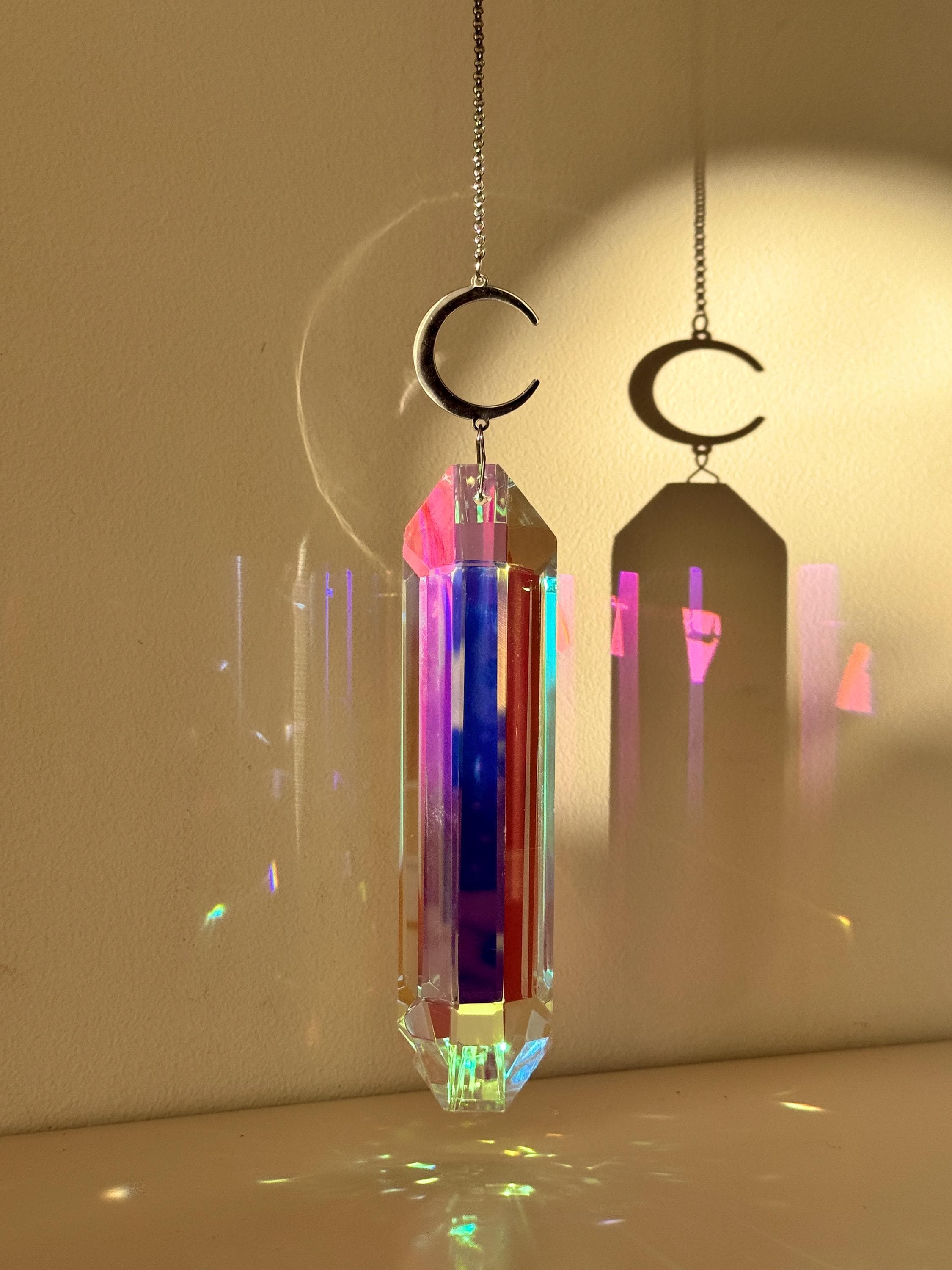 Luminescence celestial suncatcher (Sonnenfänger) with a silver crescent moon and 12 cm Aurora crystal prism scattering rainbows (Regenbogen) across a room.