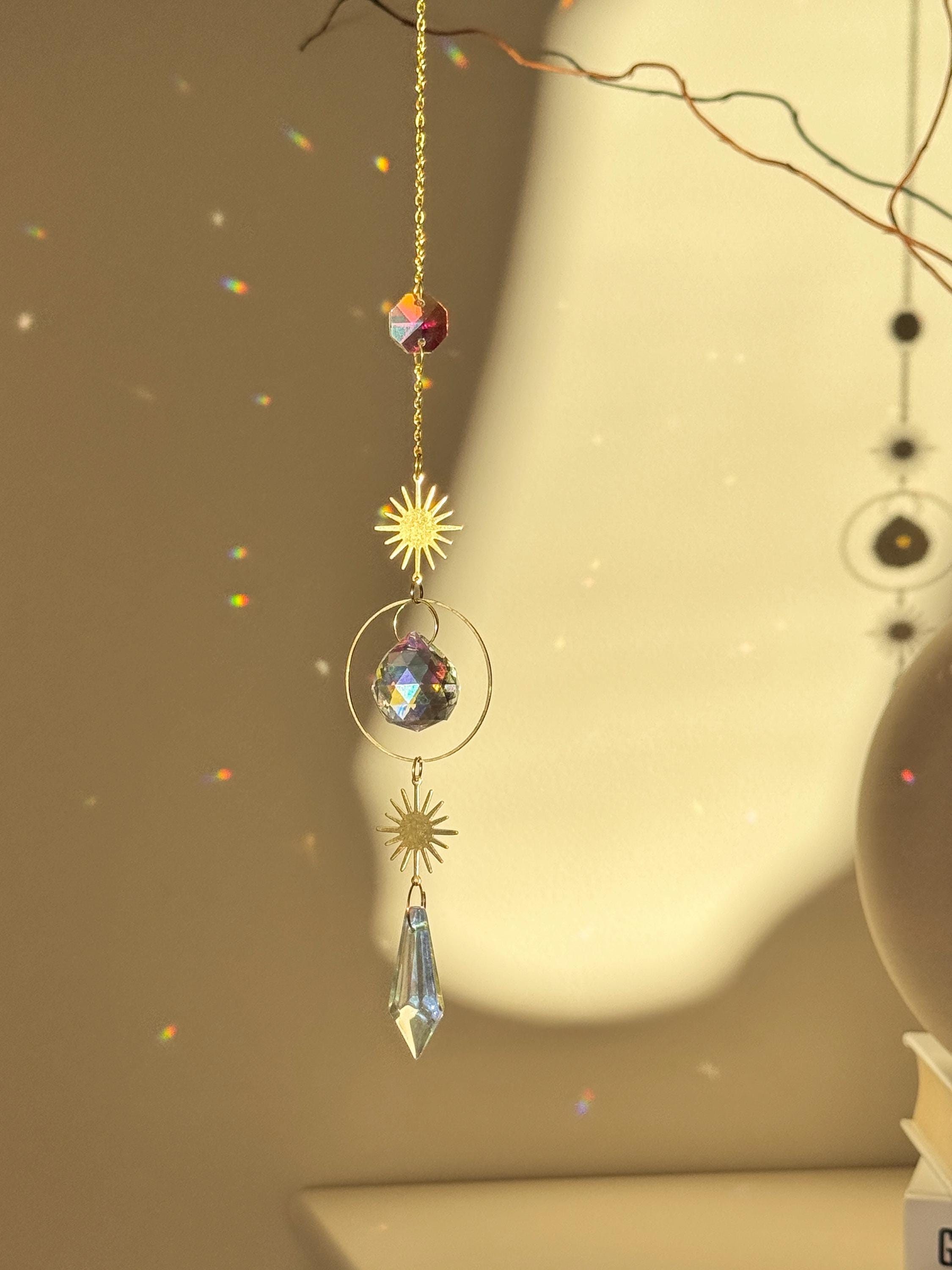 Celestial 'Sunny Days' suncatcher with gold sun charms and two crystal prisms hanging against a warm-toned wall, casting small rainbow light spots across the room.