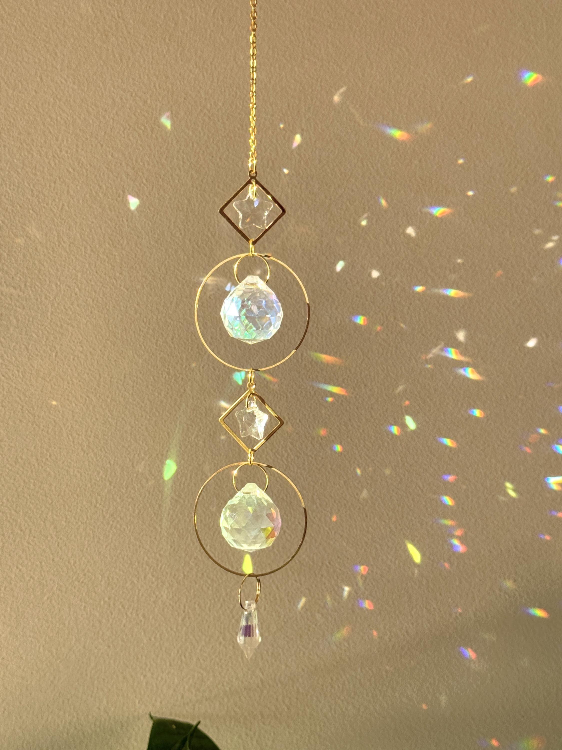 Gold hanging daydreamin suncatcher with geometric circles and prisms casting rainbow light on a wall. Sonnenfänger crystal decor for a boho home aesthetic, featuring a snake plant and shimmering Lichtreflexe.