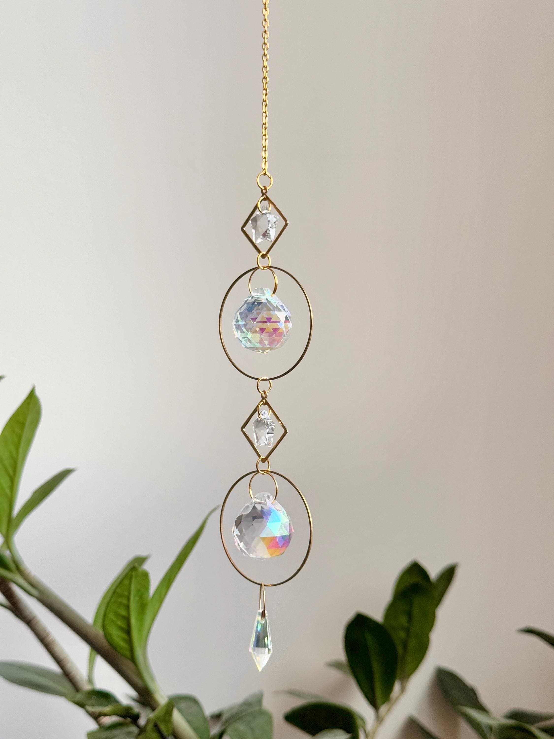 Gold hanging daydreamin suncatcher with geometric circles and prisms casting rainbow light on a wall. Sonnenfänger crystal decor for a boho home aesthetic, featuring a snake plant and shimmering Lichtreflexe.