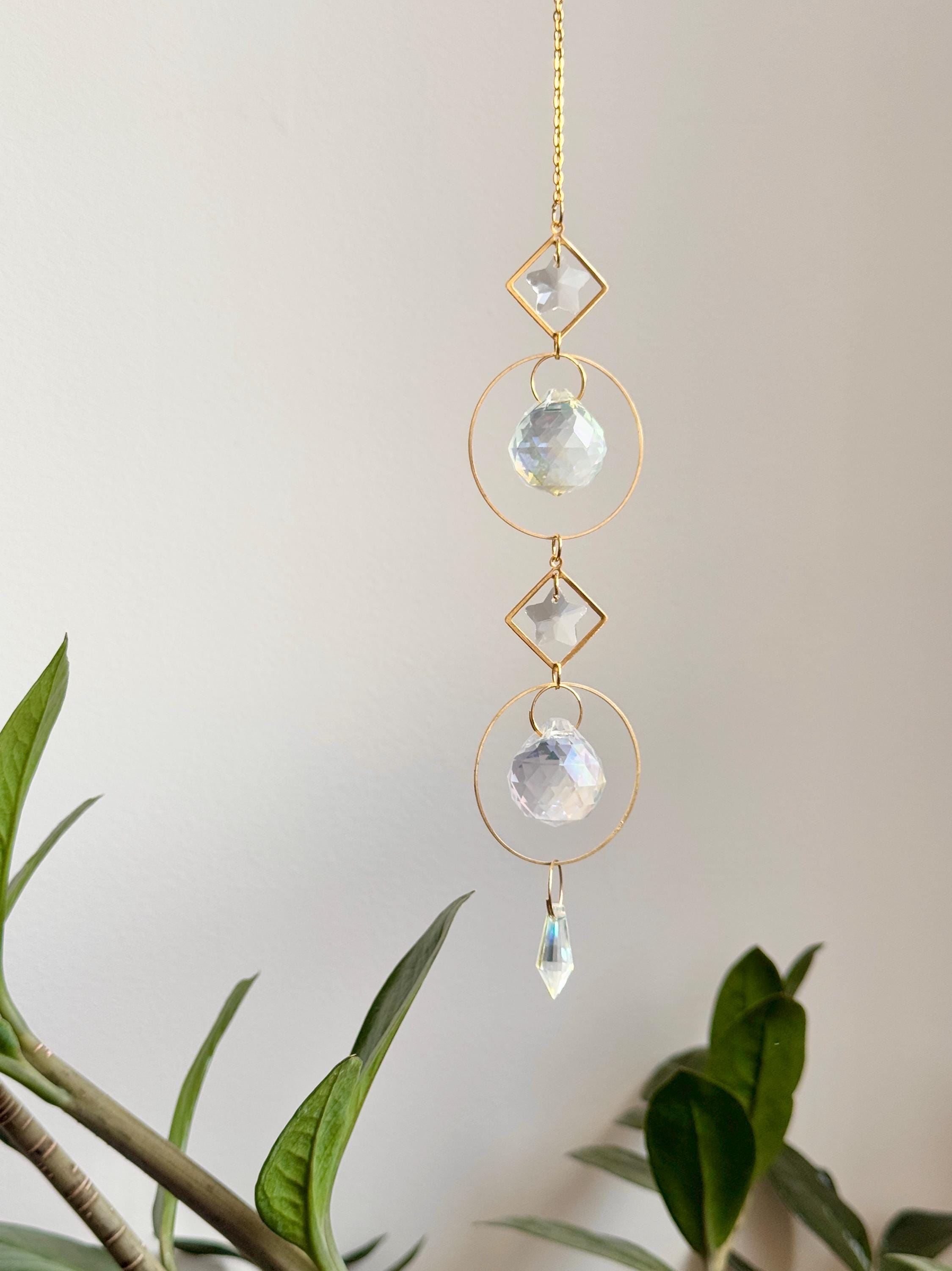 Gold hanging daydreamin suncatcher with geometric circles and prisms casting rainbow light on a wall. Sonnenfänger crystal decor for a boho home aesthetic, featuring a snake plant and shimmering Lichtreflexe.