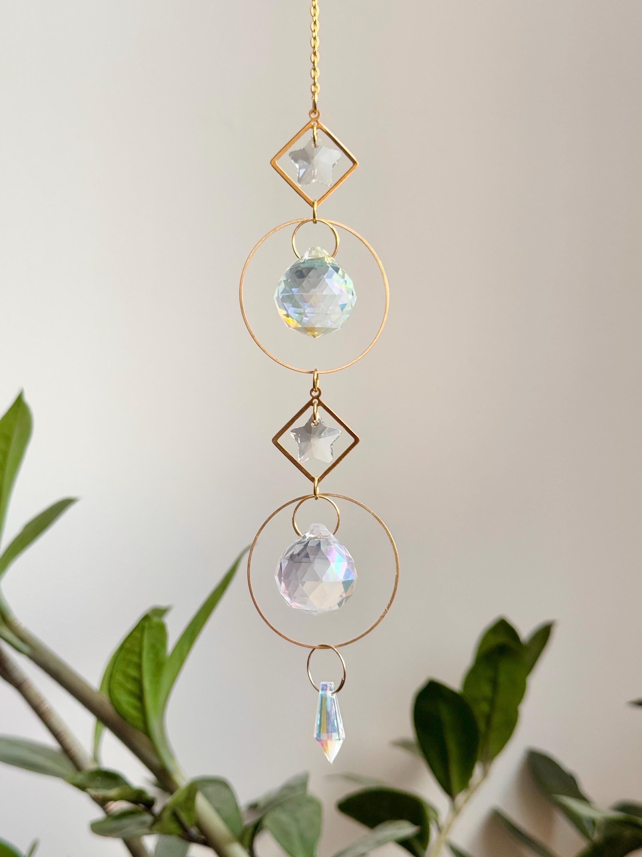 Gold hanging daydreamin suncatcher with geometric circles and prisms casting rainbow light on a wall. Sonnenfänger crystal decor for a boho home aesthetic, featuring a snake plant and shimmering Lichtreflexe.