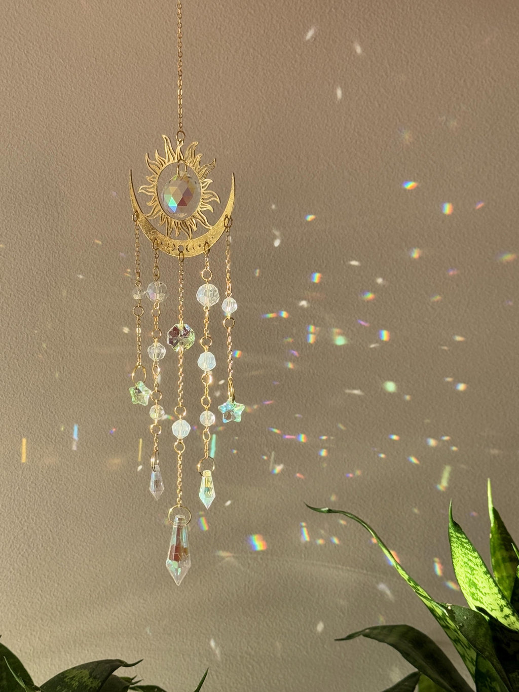 The Aura suncatcher featuring a gold crescent moon and sunburst with hanging crystal stars and prisms. Handgefertigter Sonnenfänger casting vivid rainbows on the wall. Boho-Stil Fensterdeko and magical Lichtreflexe home ornament.