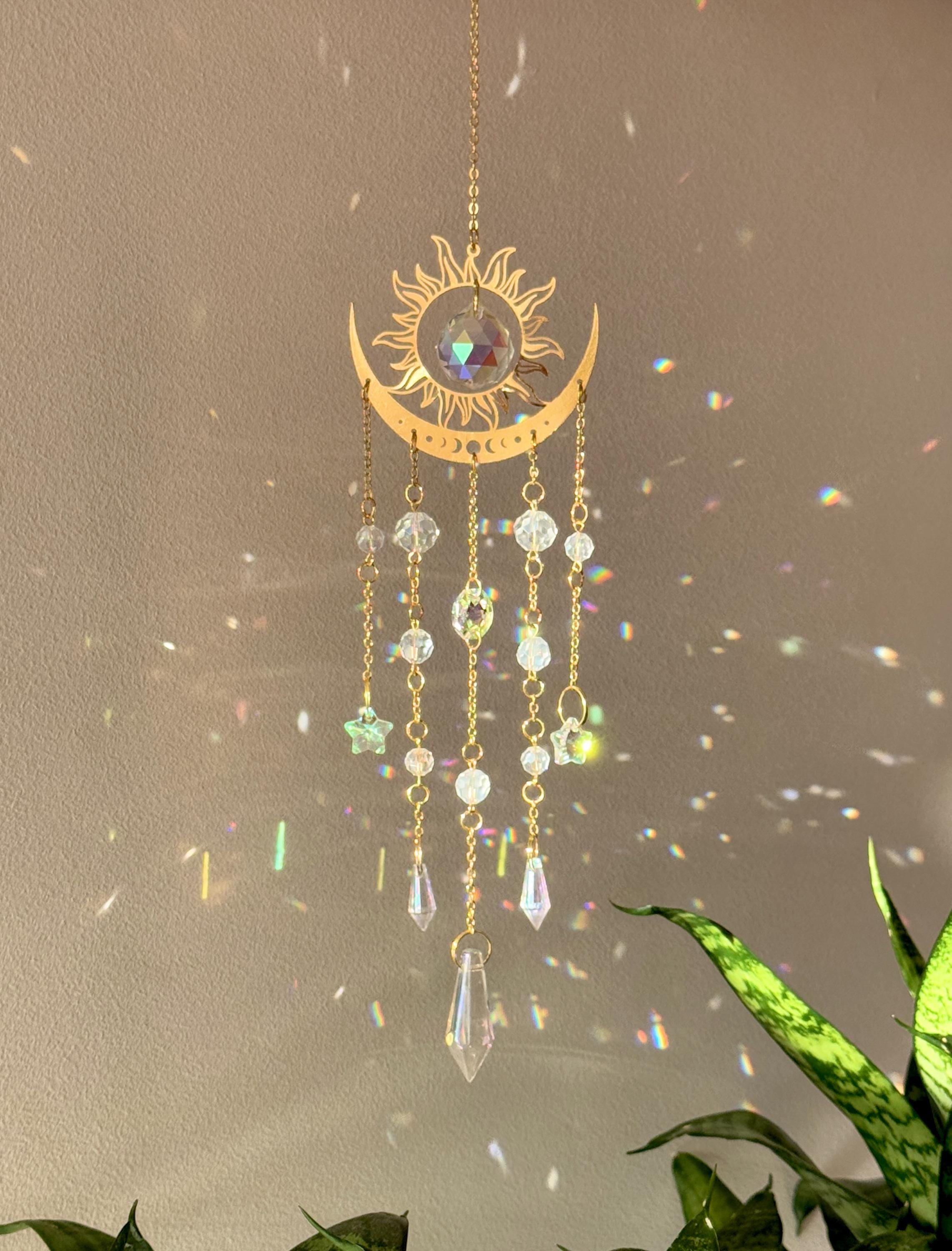 The Aura suncatcher featuring a gold crescent moon and sunburst with hanging crystal stars and prisms. Handgefertigter Sonnenfänger casting vivid rainbows on the wall. Boho-Stil Fensterdeko and magical Lichtreflexe home ornament.