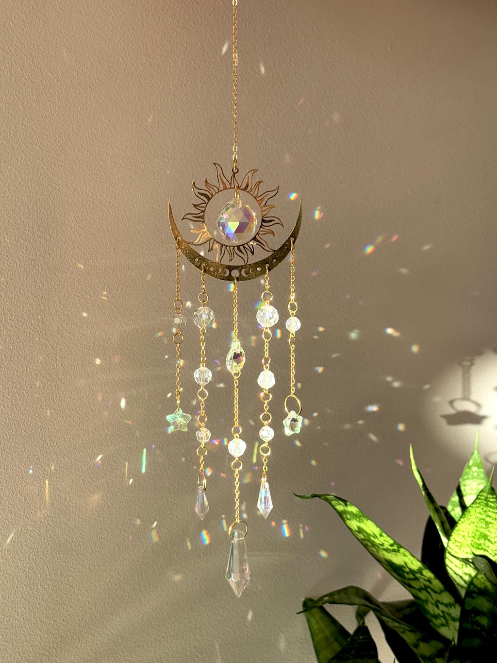 The Aura suncatcher featuring a gold crescent moon and sunburst with hanging crystal stars and prisms. Handgefertigter Sonnenfänger casting vivid rainbows on the wall. Boho-Stil Fensterdeko and magical Lichtreflexe home ornament.