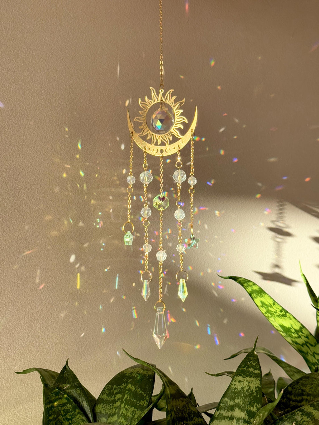 The Aura suncatcher featuring a gold crescent moon and sunburst with hanging crystal stars and prisms. Handgefertigter Sonnenfänger casting vivid rainbows on the wall. Boho-Stil Fensterdeko and magical Lichtreflexe home ornament.