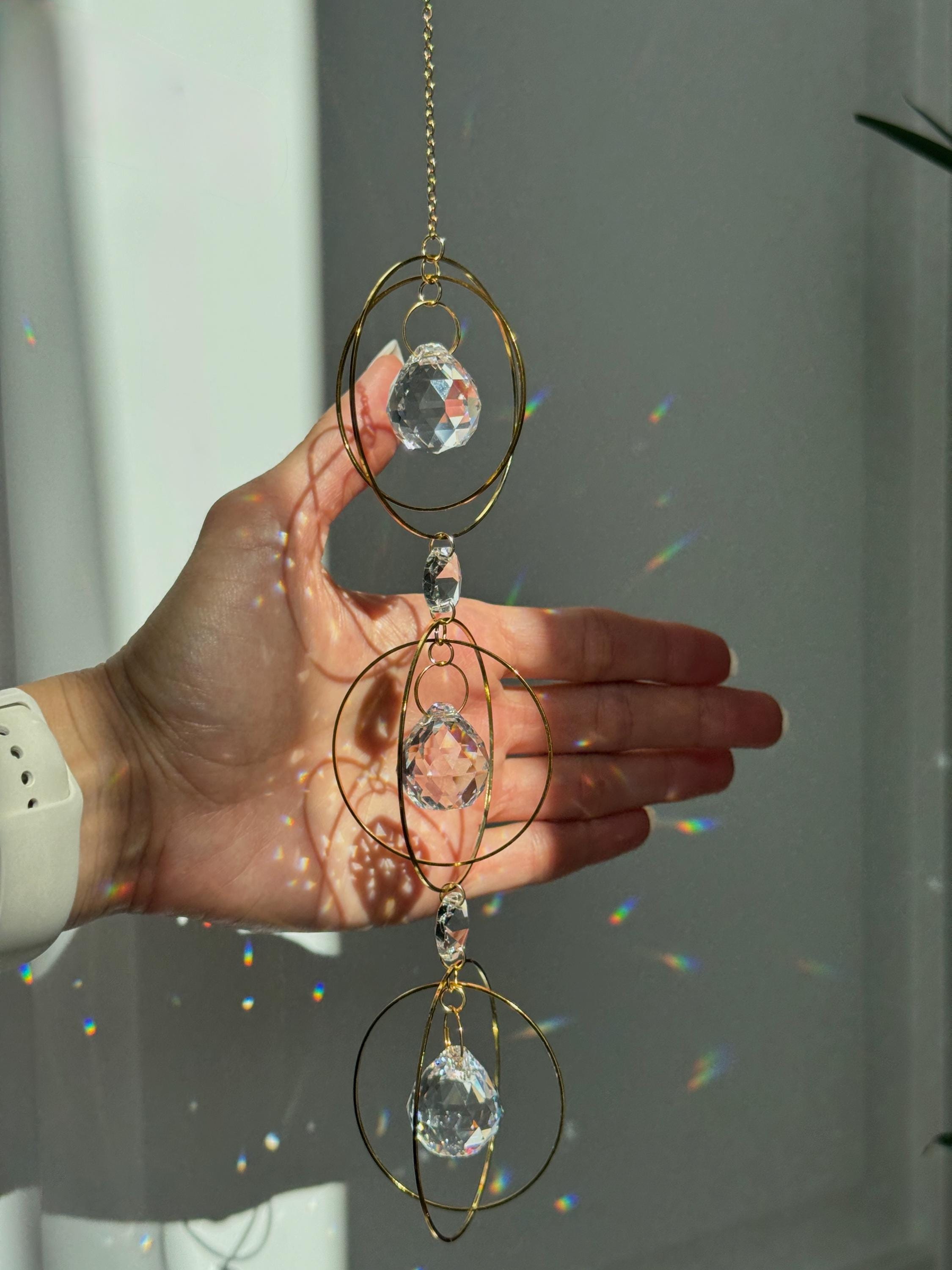 Bestselling Trinity suncatcher with triple gold circles and faceted crystals. Handgefertigter Sonnenfänger creating intense rainbow patterns on a white background. Boho-Stil window decoration and premium Lichtreflexe crystal ornament.
