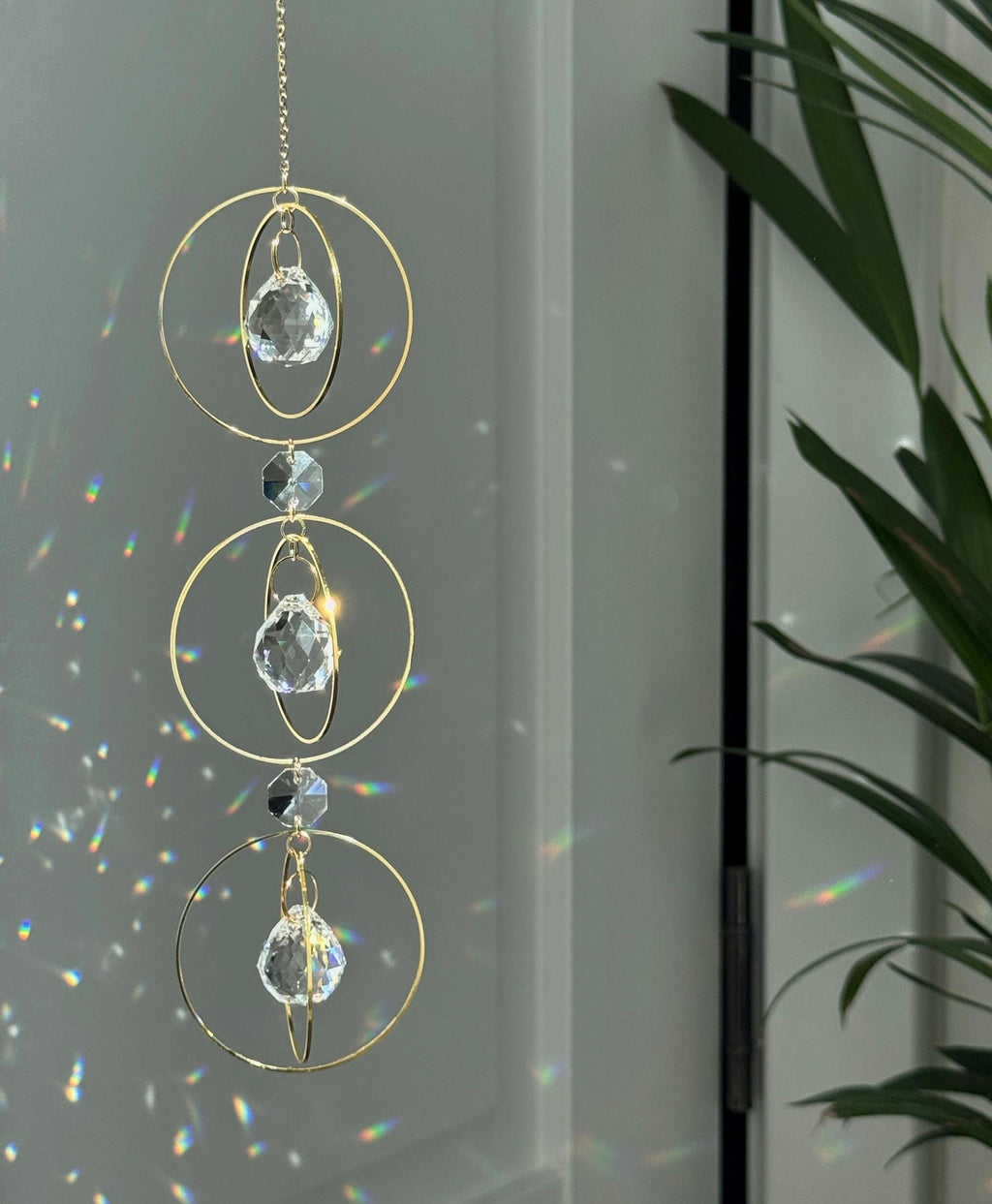 Bestselling Trinity suncatcher with triple gold circles and faceted crystals. Handgefertigter Sonnenfänger creating intense rainbow patterns on a white background. Boho-Stil window decoration and premium Lichtreflexe crystal ornament.
