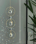 Bestselling Trinity suncatcher with triple gold circles and faceted crystals. Handgefertigter Sonnenfänger creating intense rainbow patterns on a white background. Boho-Stil window decoration and premium Lichtreflexe crystal ornament.