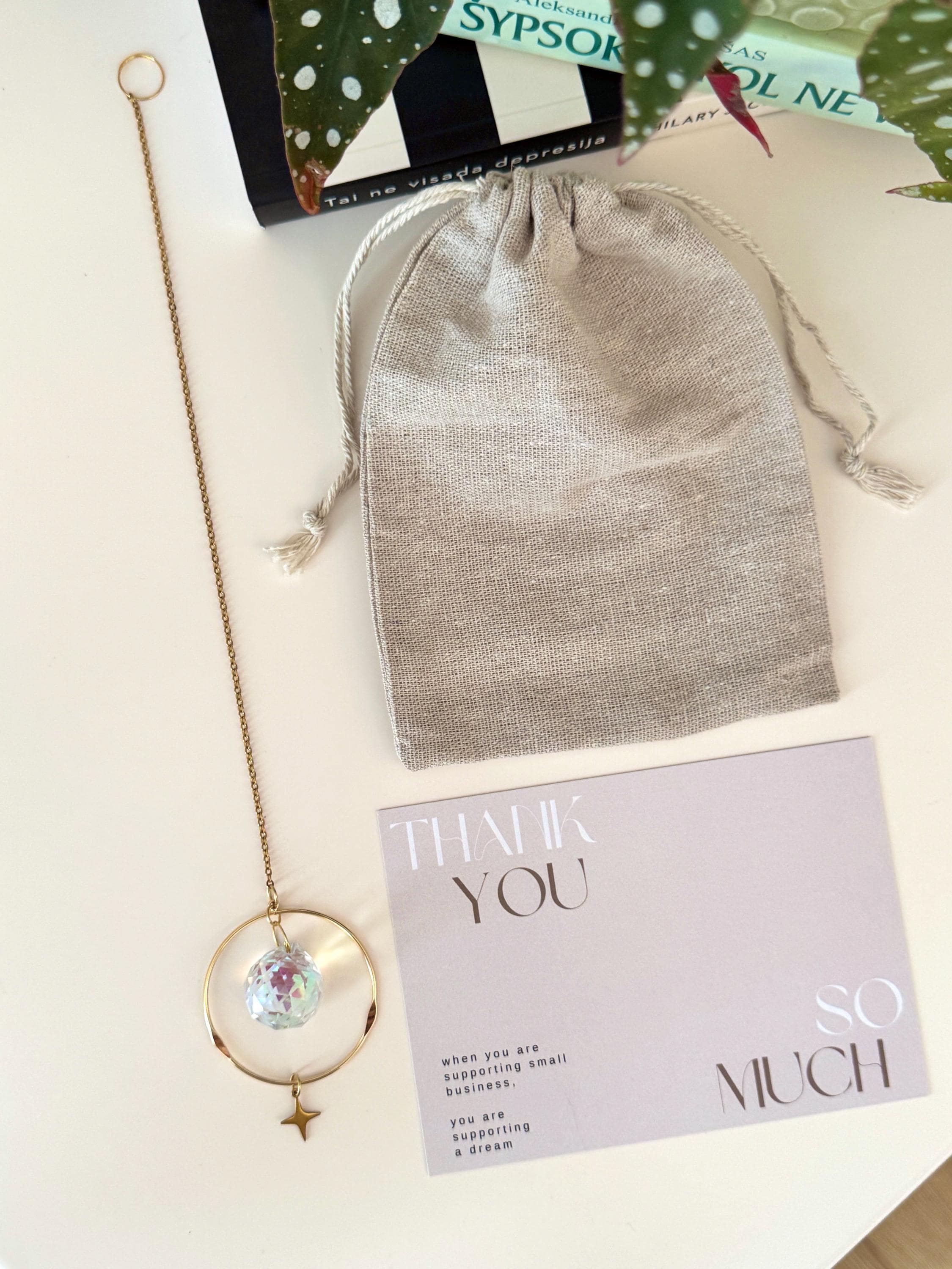 Celestial Compass suncatcher (Sonnenfänger) with a gold wavy brass ring,  crystal prism, and star charm, reflecting rainbows (Regenbogen) on a white wall.