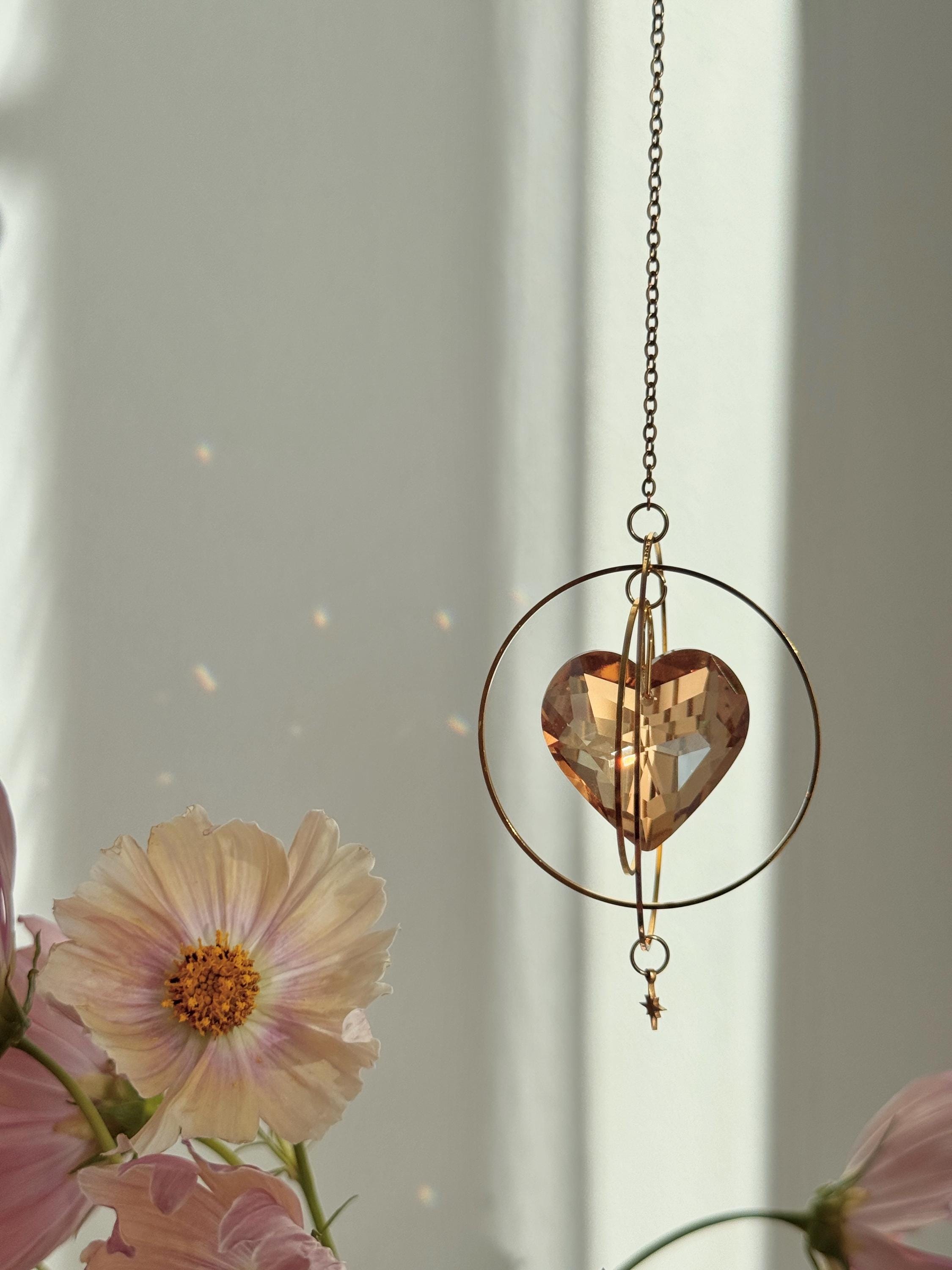 Sunkissed Heartbeat crystal suncatcher featuring a warm amber-gold faceted heart prism. Handmade celestial window decor with gold rings casting rainbow light flares (Sonnenfänger).