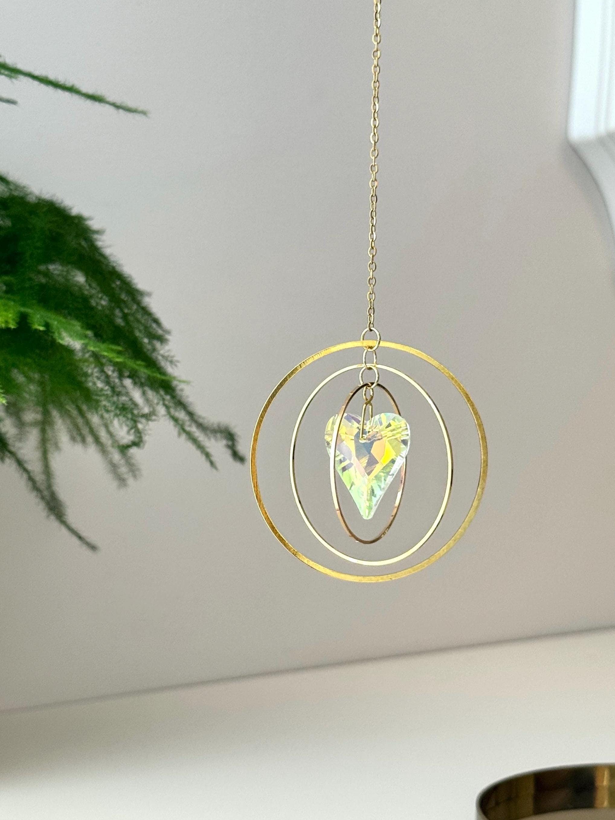 Handcrafted Sunkissed Heartbeat suncatcher with a faceted crystal heart and gold rings casting vibrant rainbows on a white wall.