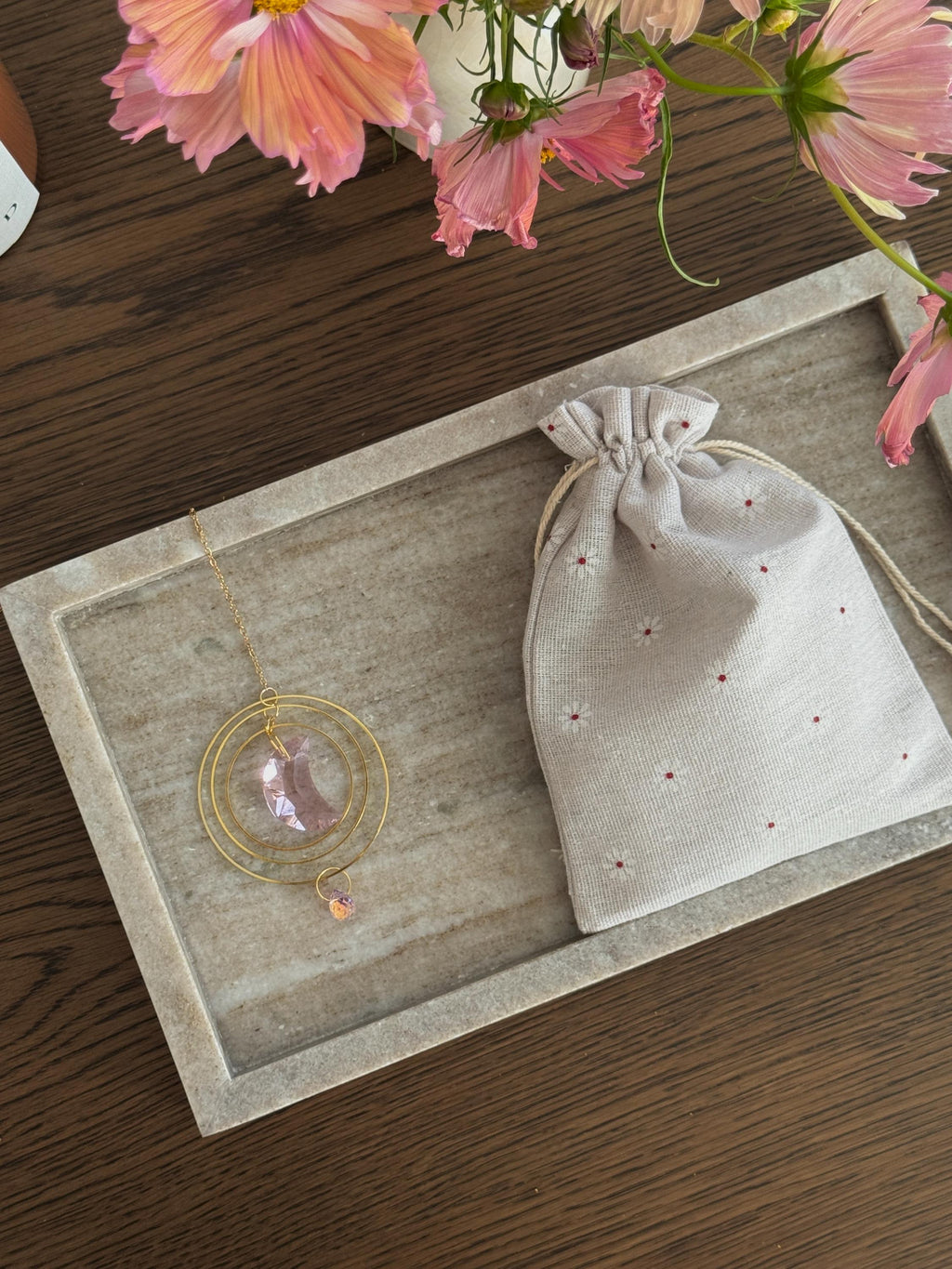 Suncatcher with a drawstring bag on a wooden surface with pink flowers in the background