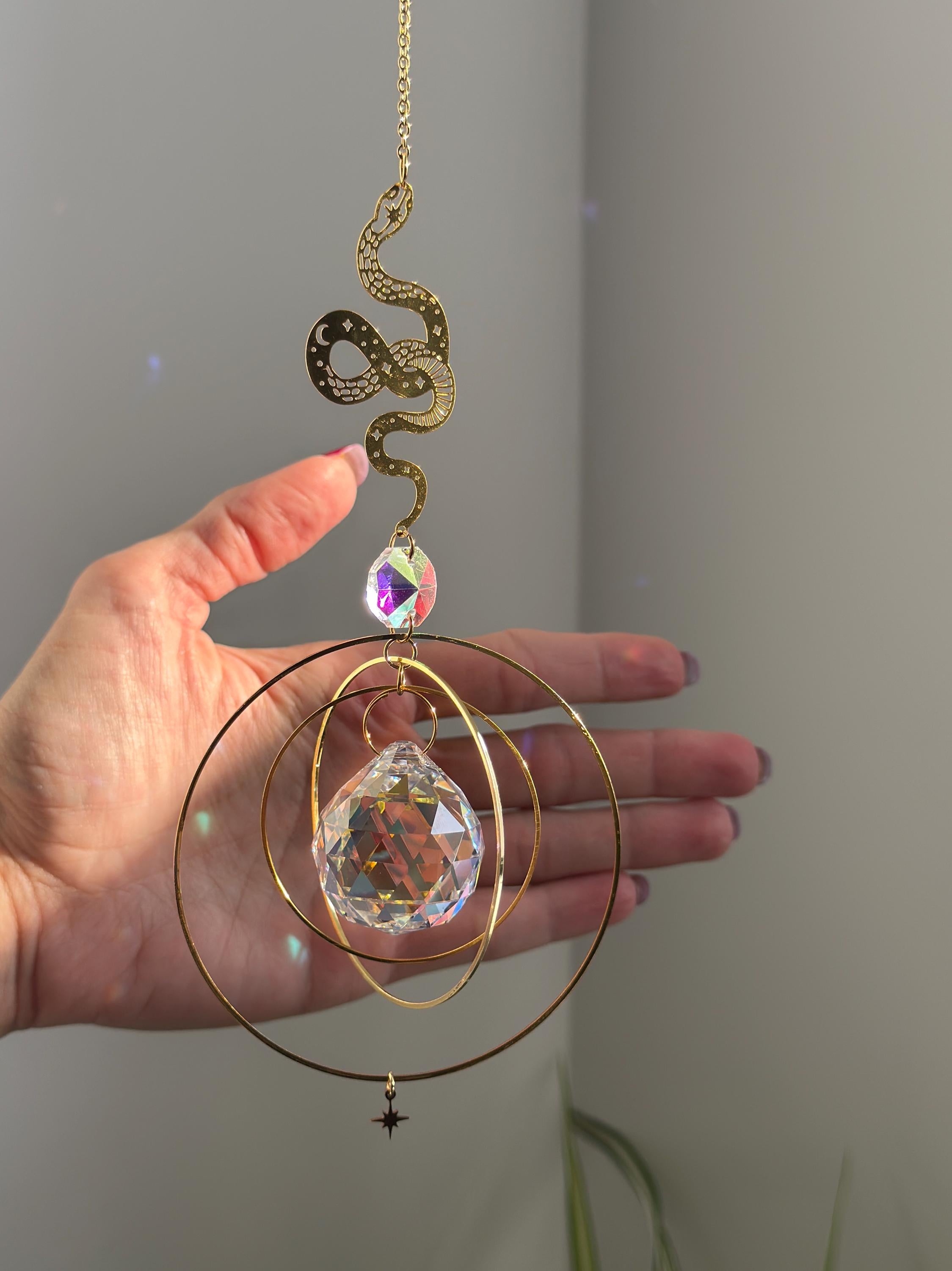Handcrafted Sunkissed Heartbeat suncatcher with a faceted crystal heart and gold orbital rings near a hand