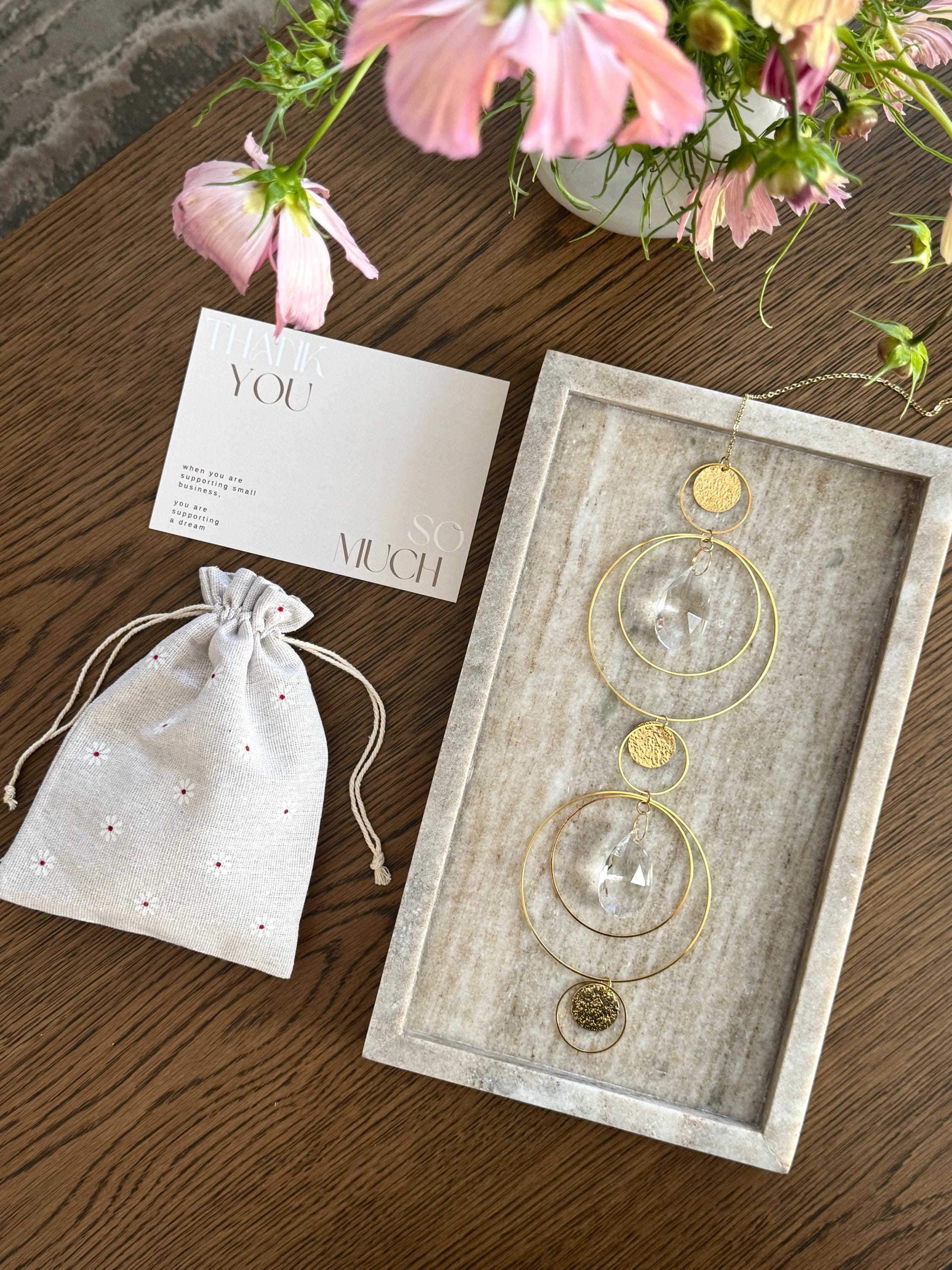 Symmetry in light suncatcher on a stone tray with a linen drawstring bag and pink flowers in the background
