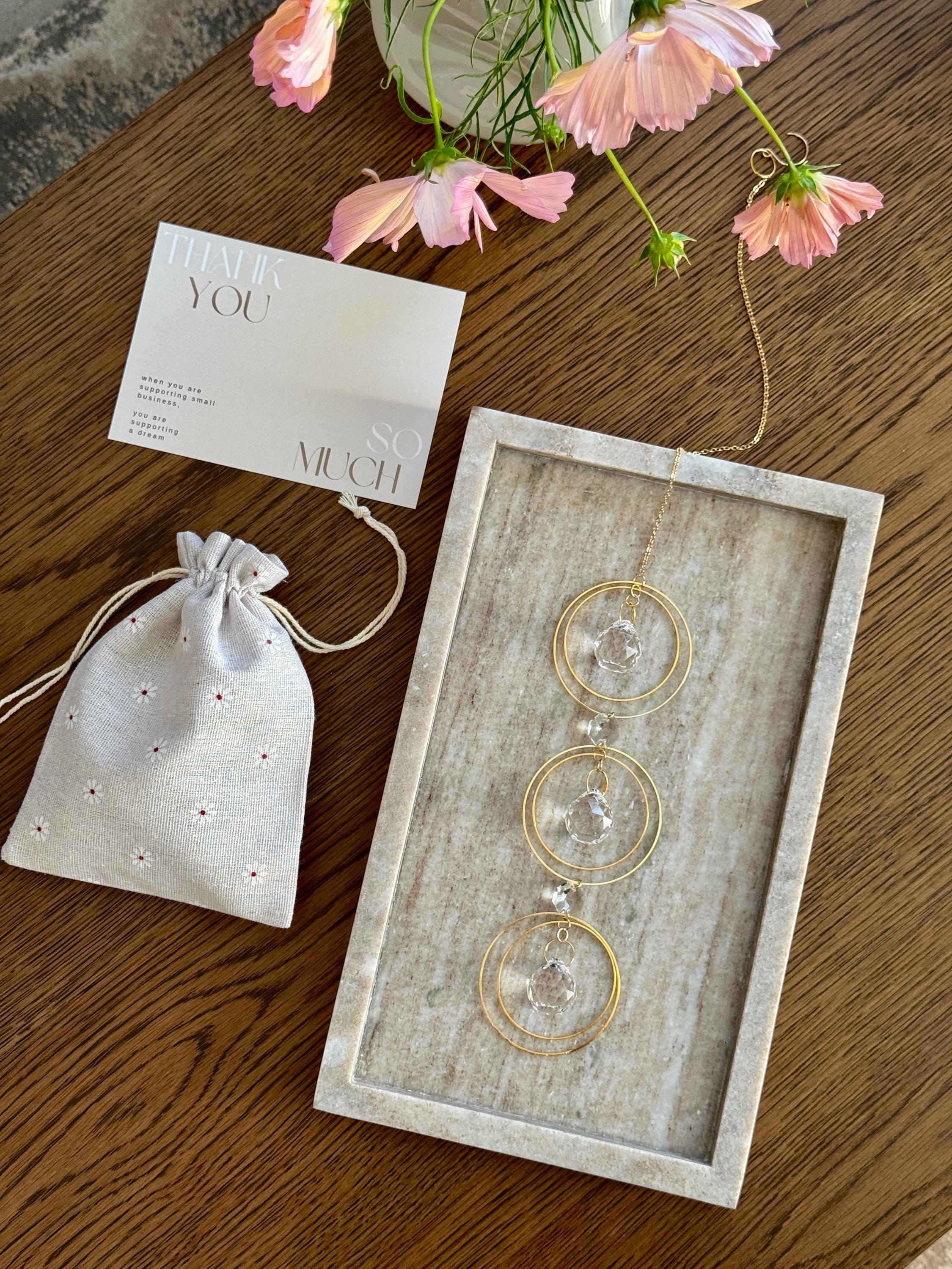 Bestselling Trinity suncatcher with triple gold circles and faceted crystals. Handgefertigter Sonnenfänger creating intense rainbow patterns on a white background. Boho-Stil window decoration and premium Lichtreflexe crystal ornament.