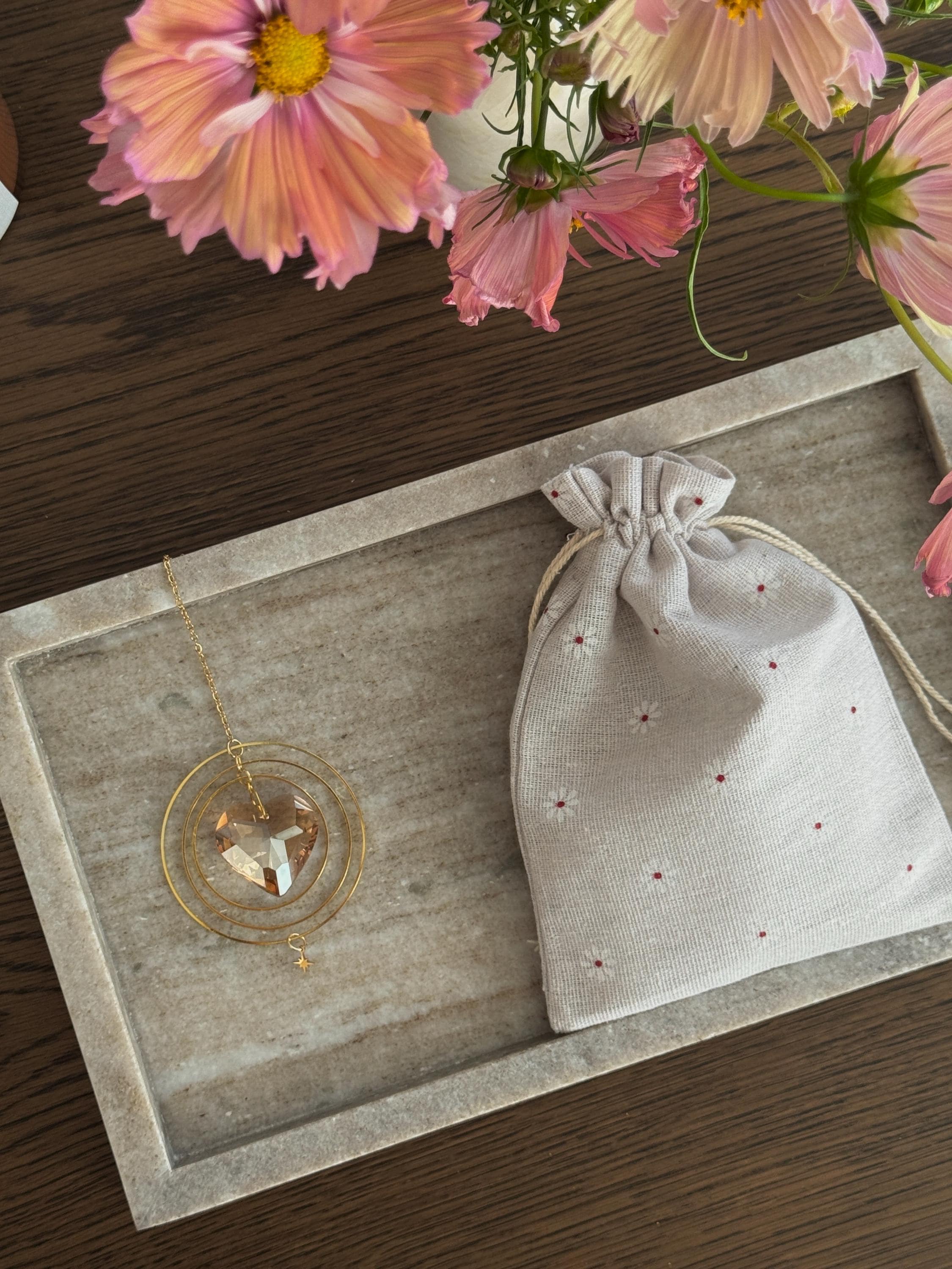 heart shaped suncatcher on a stone tray with a linen drawstring bag and pink flowers in the background