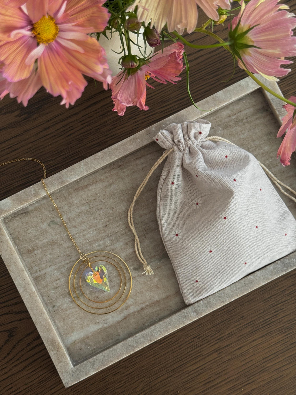 Heart shaped suncatcher and decorative linen bag on a wooden surface with flowers in the background.