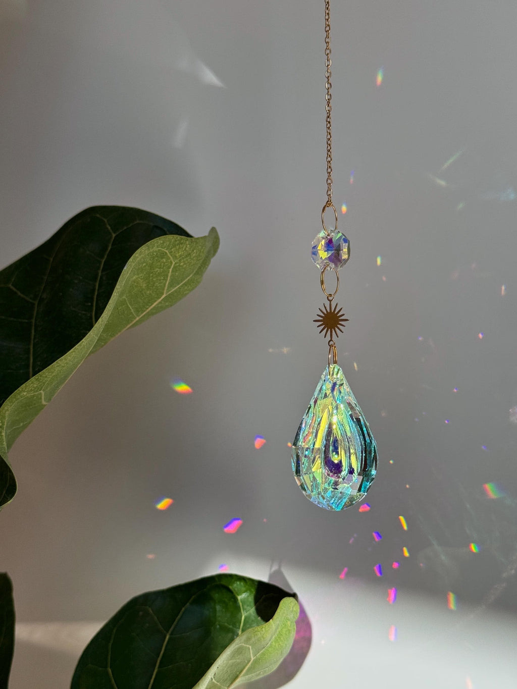 Celestial Droplet suncatcher (Sonnenfänger) with a 4cm teardrop crystal prism reflecting vibrant rainbows (Regenbogen) on a bright interior wall.
