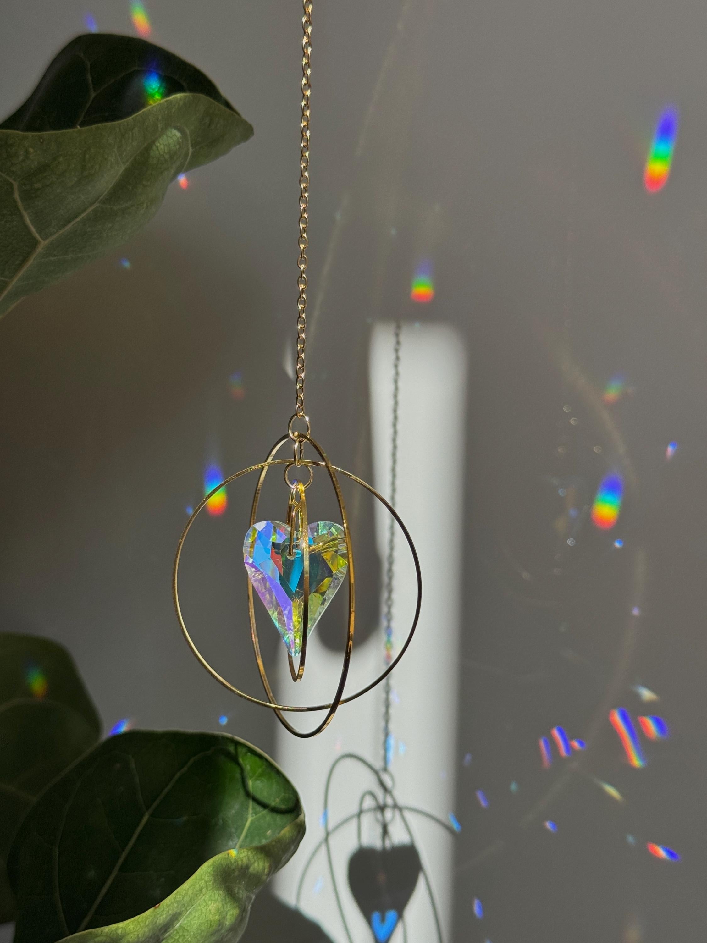 Handcrafted Sunkissed Heartbeat suncatcher with a faceted crystal heart and gold rings casting vibrant rainbows on a white wall.