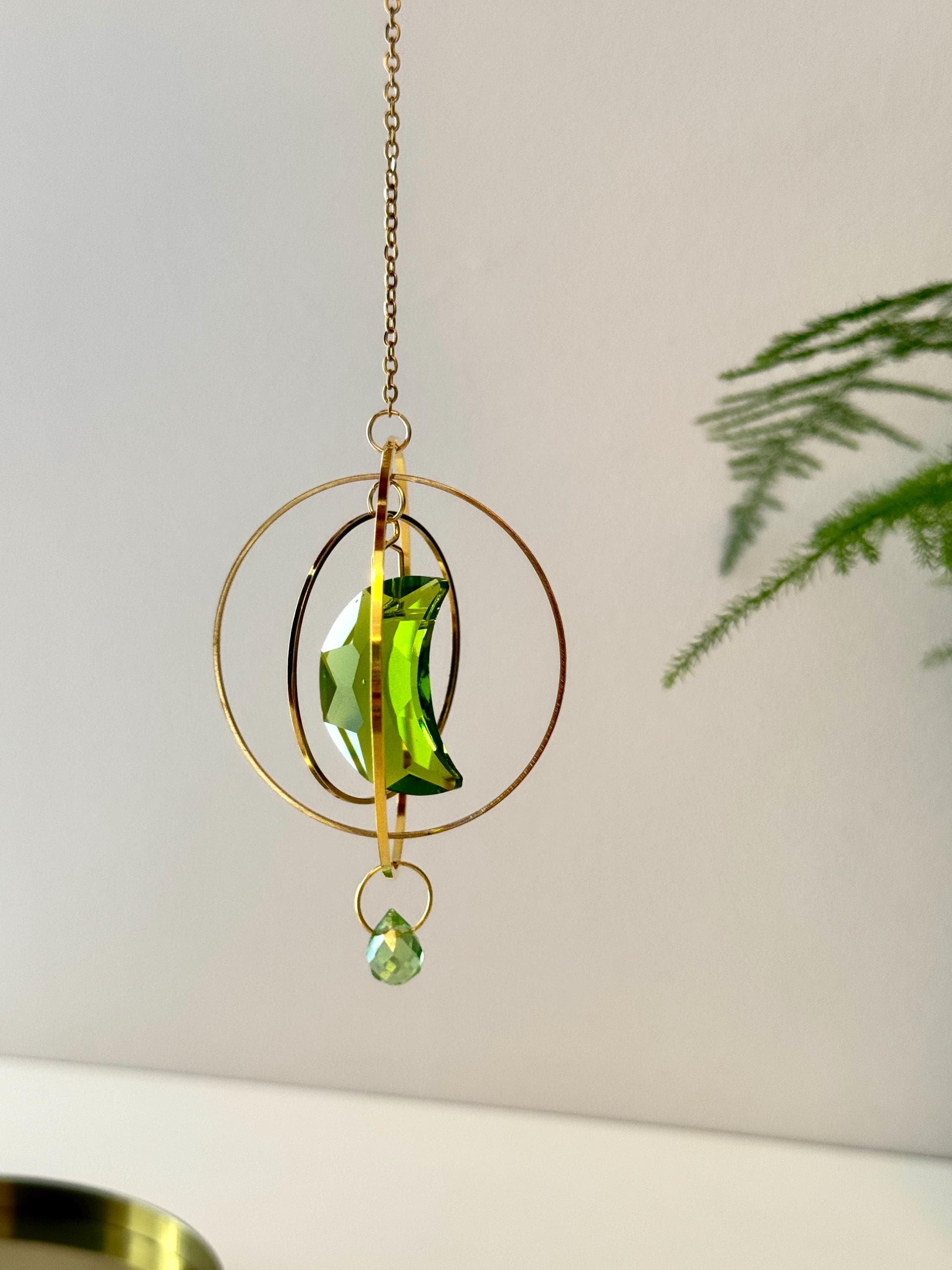 Handmade green crescent moon crystal suncatcher "Over the Moon" casting magical rainbows on a wall. Celestial gold ring window decor and rainbow maker (Sonnenfänger)