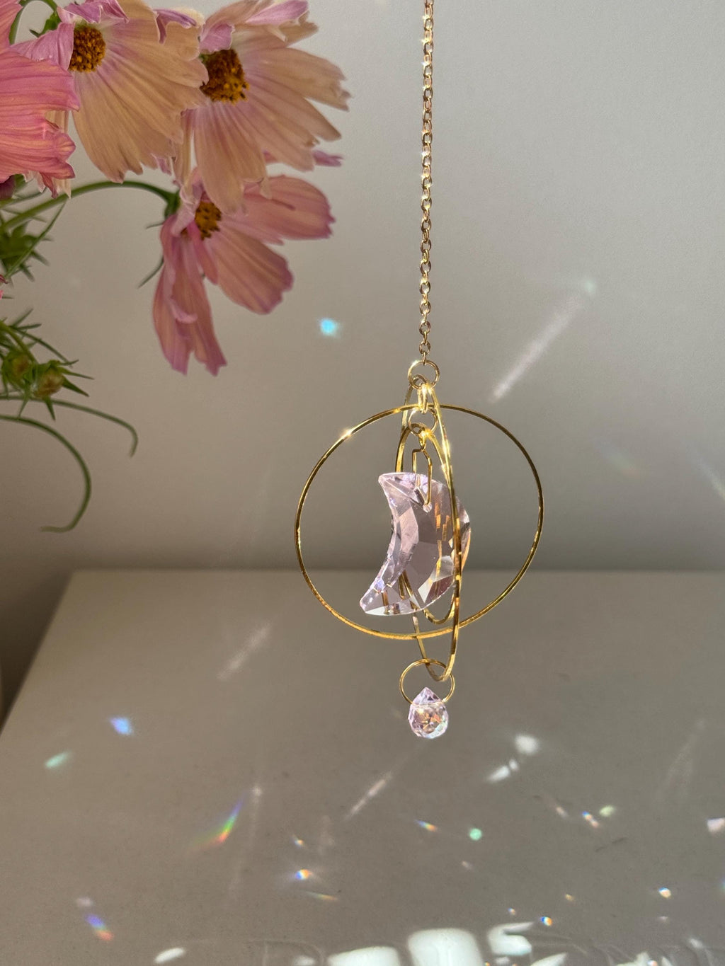 Handmade pink crescent moon suncatcher hanging in a sunny window creating rainbow prisms on the wall