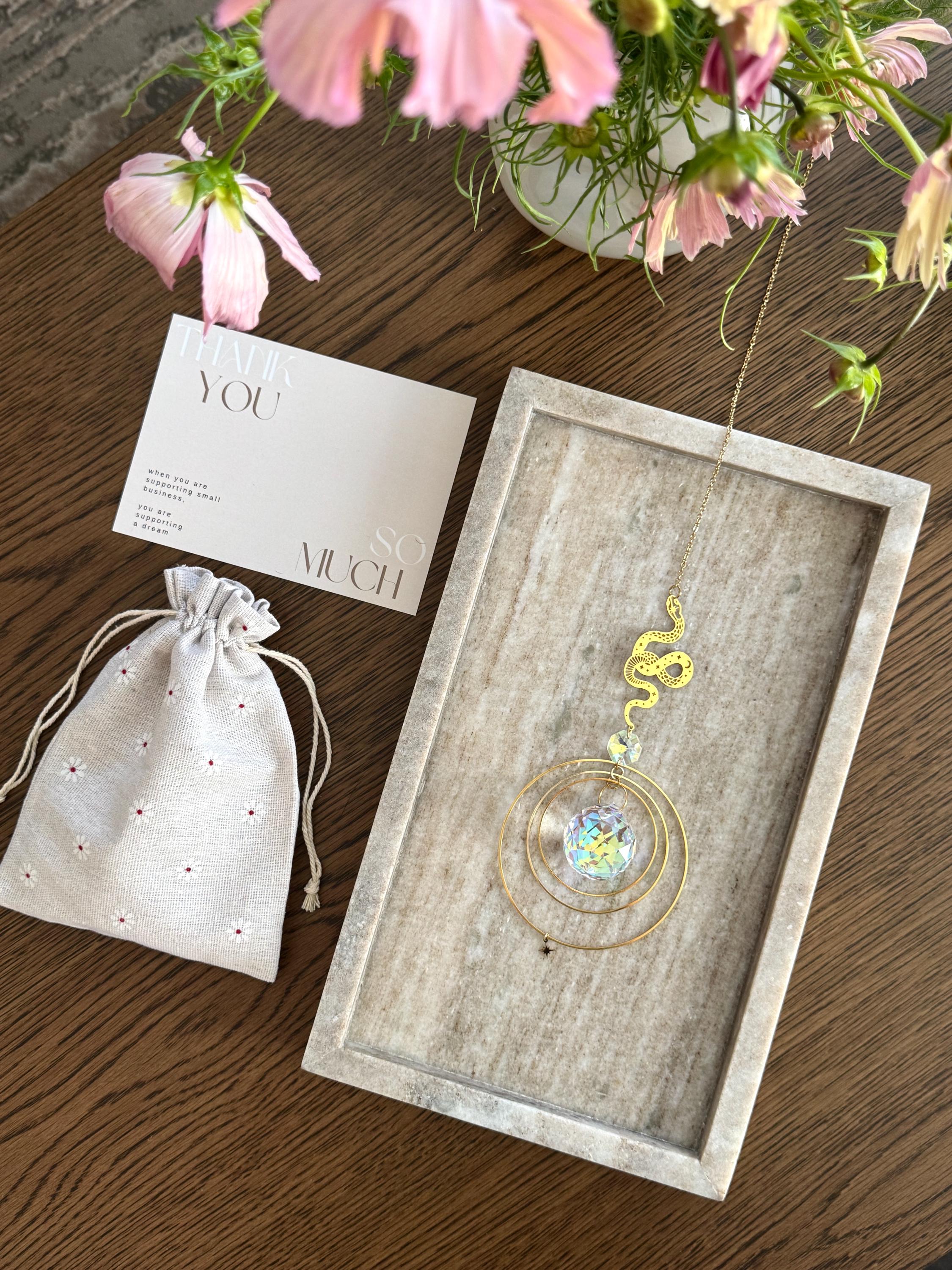Crystal suncatcher near a linen drawstring pouch, and flowers on a wooden surface
