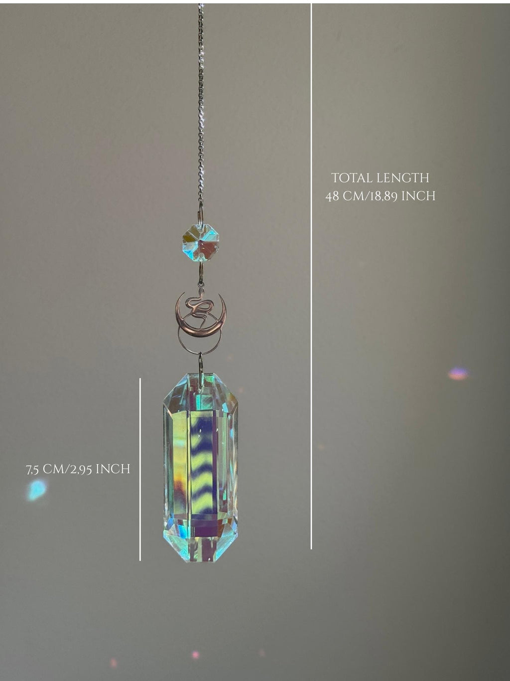 Close-up of the intricate snake charm and faceted crystal obelisk (Kristall) against a sunlit window background.