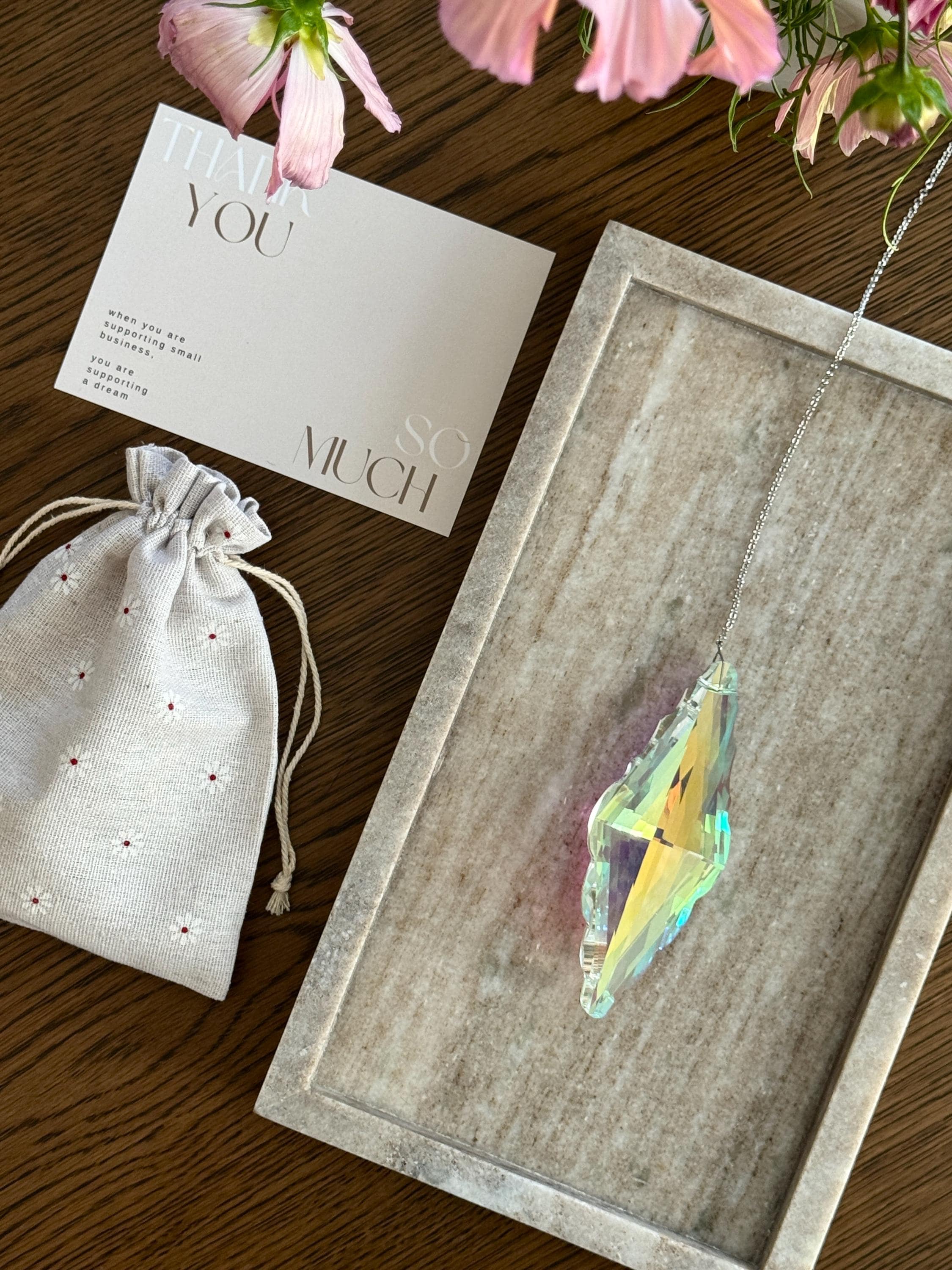 Crystal pendant on a wooden tray with a card and drawstring bag on a wooden surface.