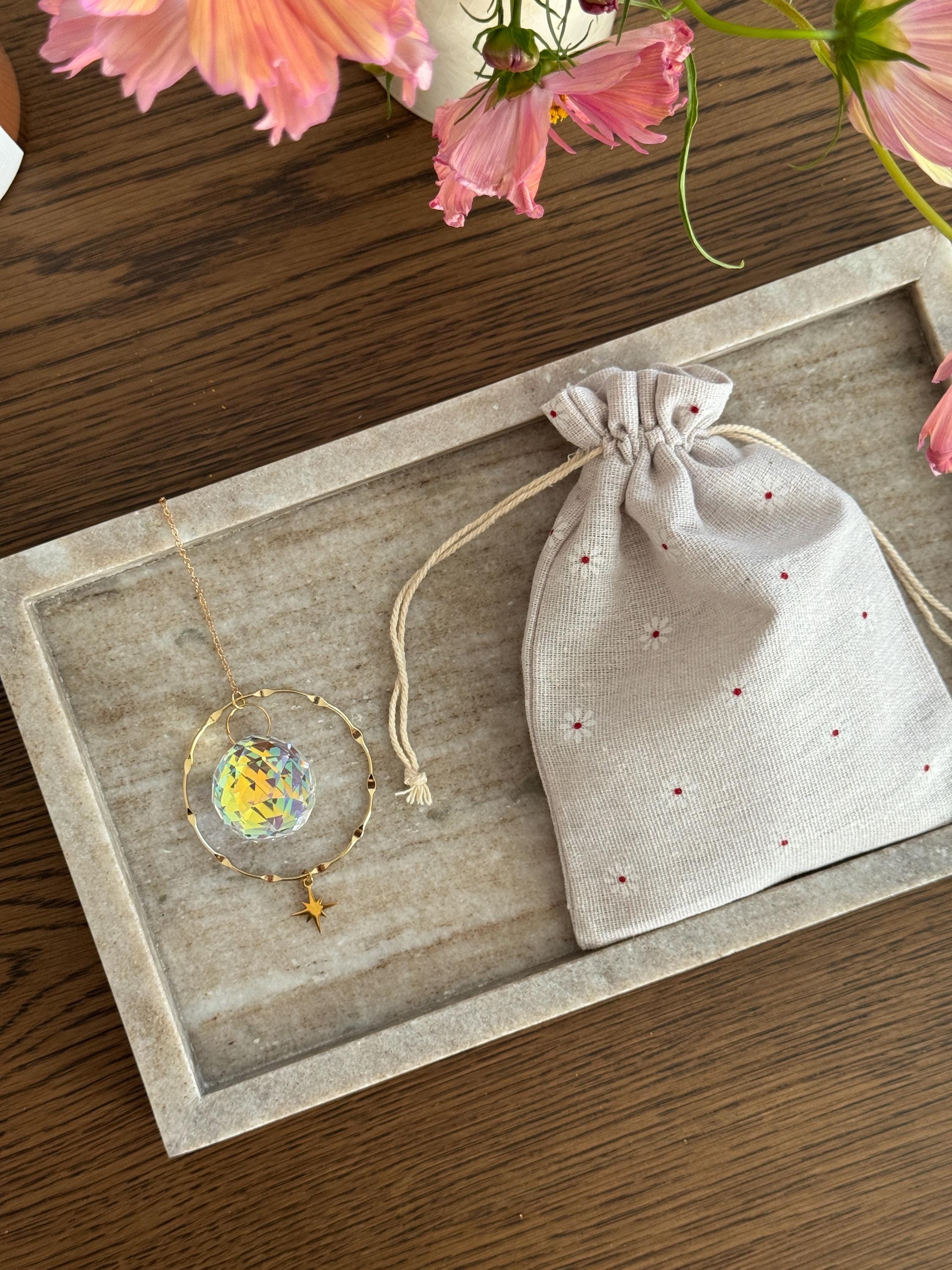 Suncacther with a linen drawstring bag on a wooden surface with flowers in the background