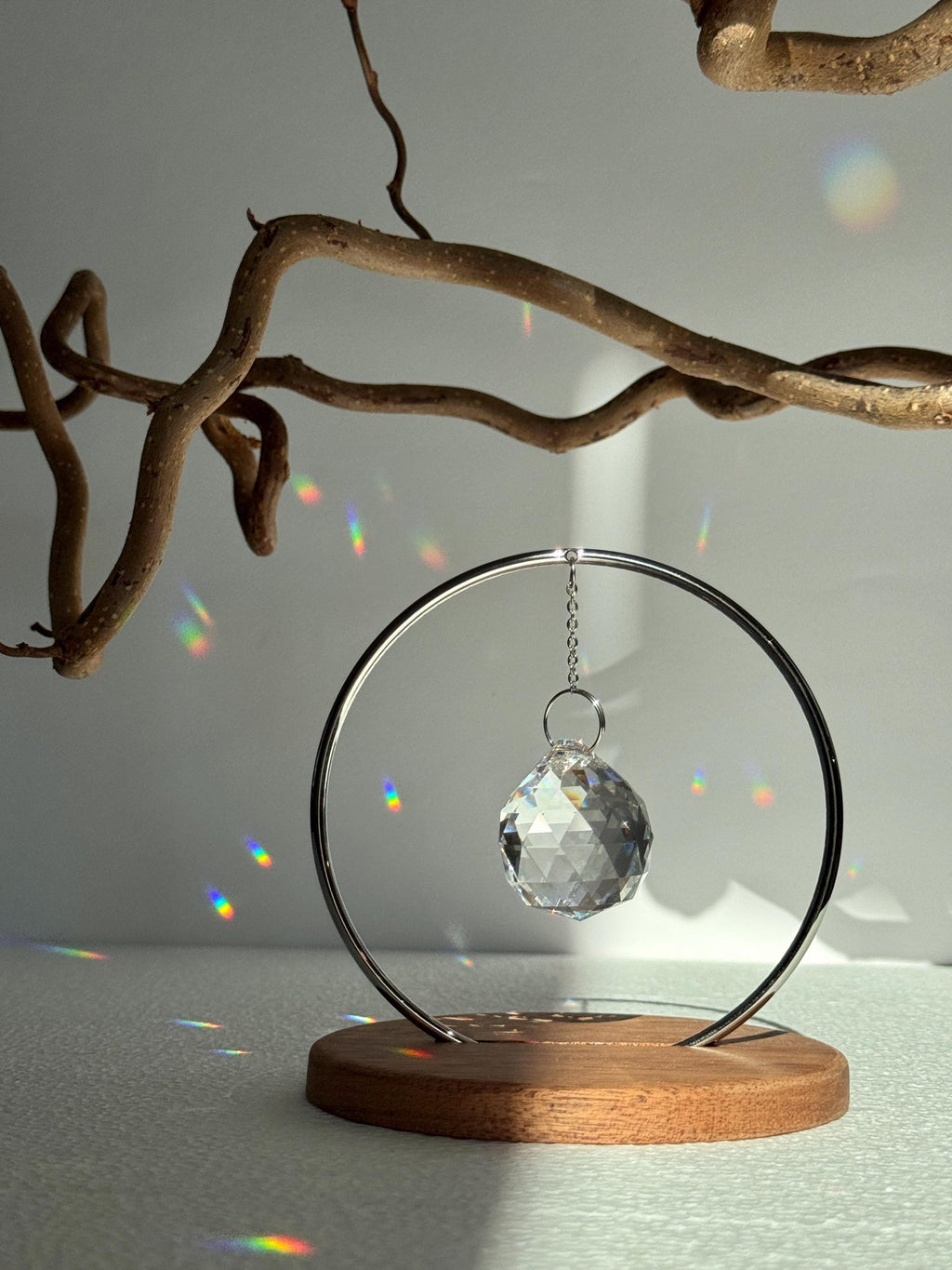 The Circle tabletop suncatcher featuring a silver stainless steel ring and faceted crystal prism casting vibrant rainbows on a white surface.