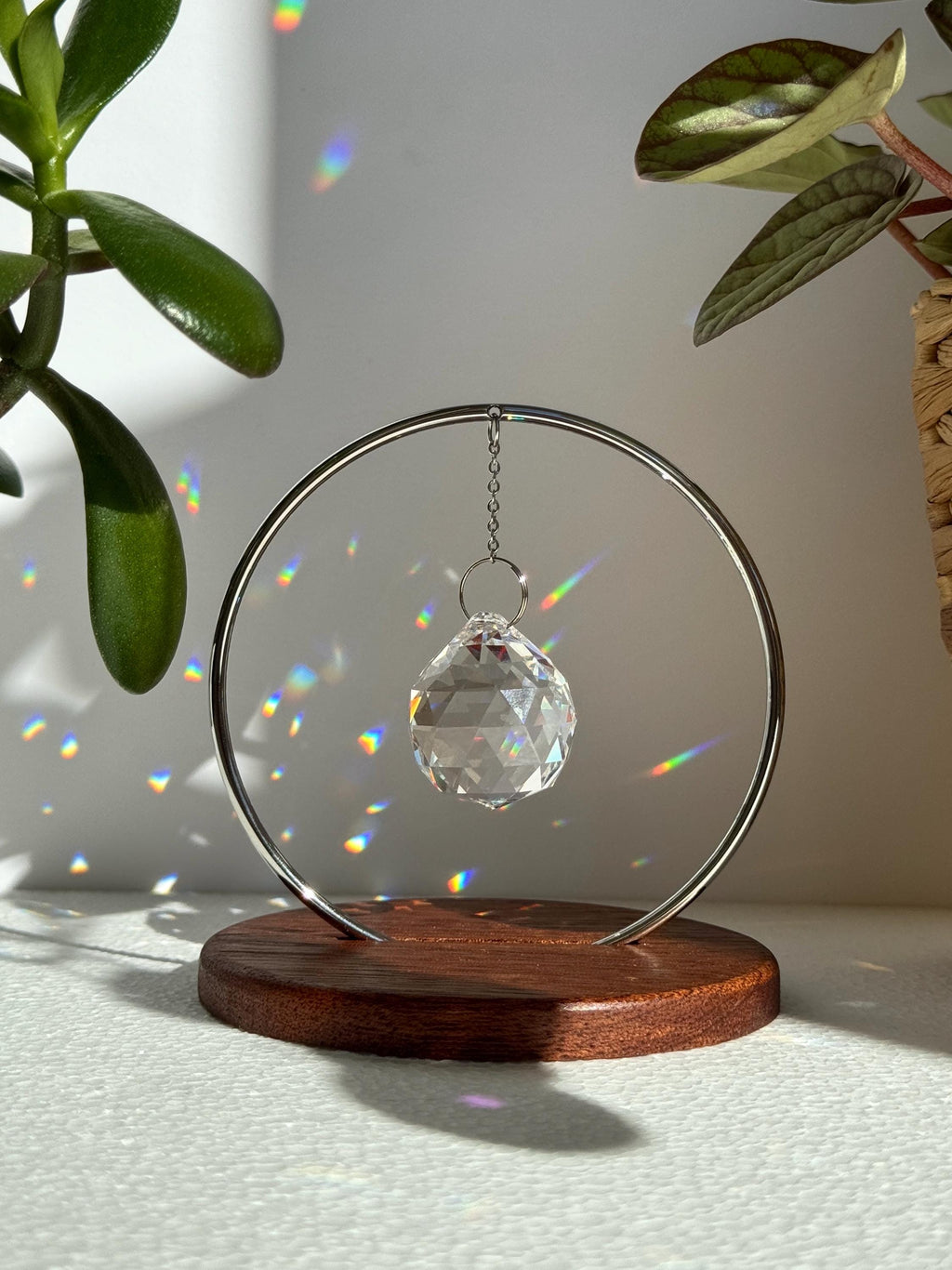 The Circle tabletop suncatcher featuring a silver stainless steel ring and faceted crystal prism casting vibrant rainbows on a white surface.