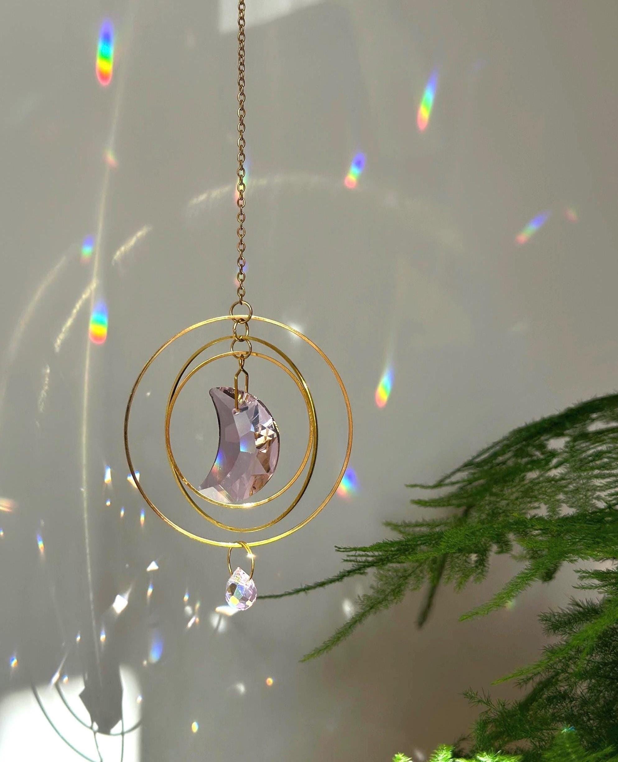 Handmade pink crescent moon suncatcher hanging in a sunny window creating rainbow prisms on the wall