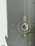 The "North Star Prism" celestial suncatcher with a clear, high-quality faceted round crystal sphere. It features a smaller octagonal crystal bead and a sharp four-pointed gold star charm hanging below, reflecting brilliant light patterns on the wall behind.