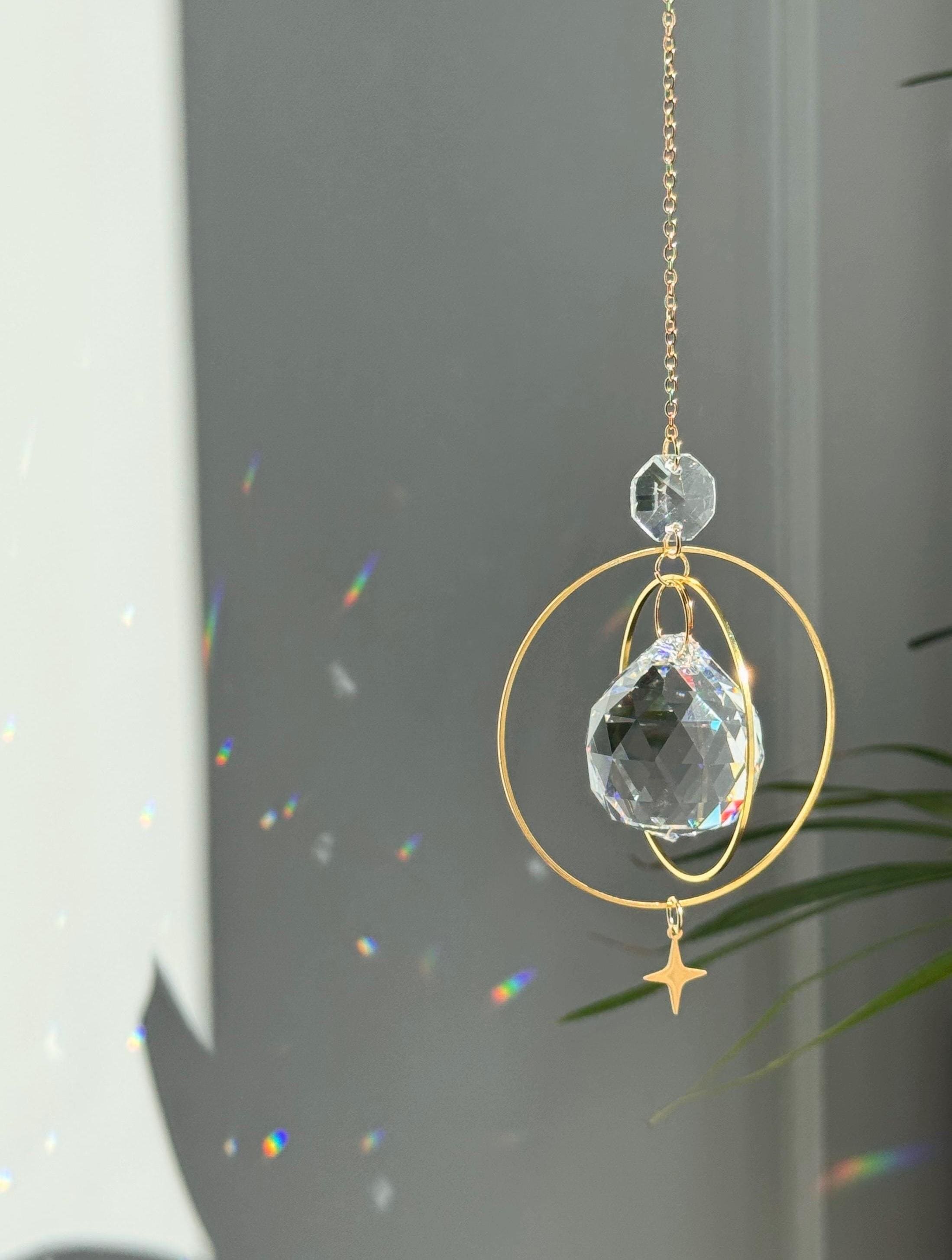 The "North Star Prism" celestial suncatcher with a clear, high-quality faceted round crystal sphere. It features a smaller octagonal crystal bead and a sharp four-pointed gold star charm hanging below, reflecting brilliant light patterns on the wall behind.