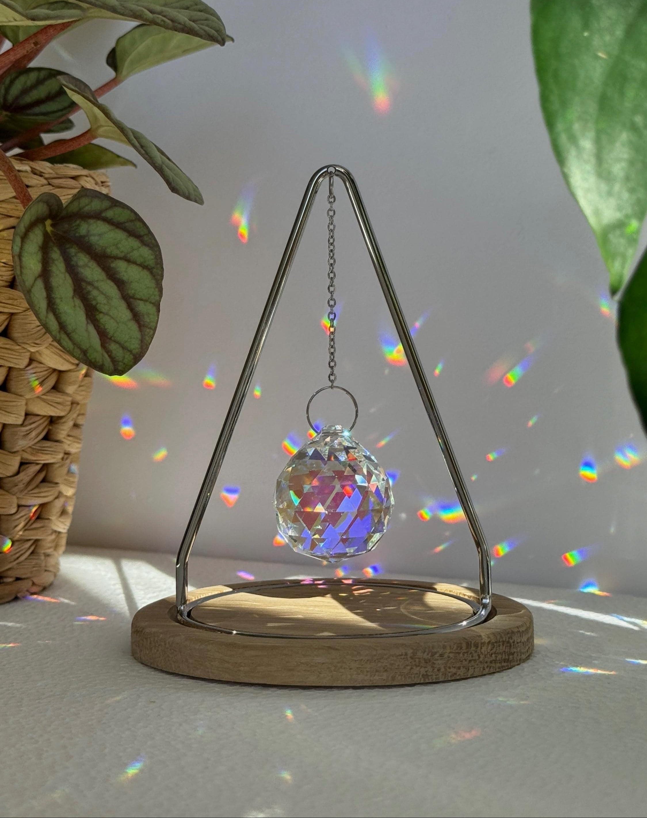 The Triangle Sonnenfänger: A modern crystal prism suncatcher with a handcrafted oak wood base and stainless steel frame, creating magical rainbow reflections.