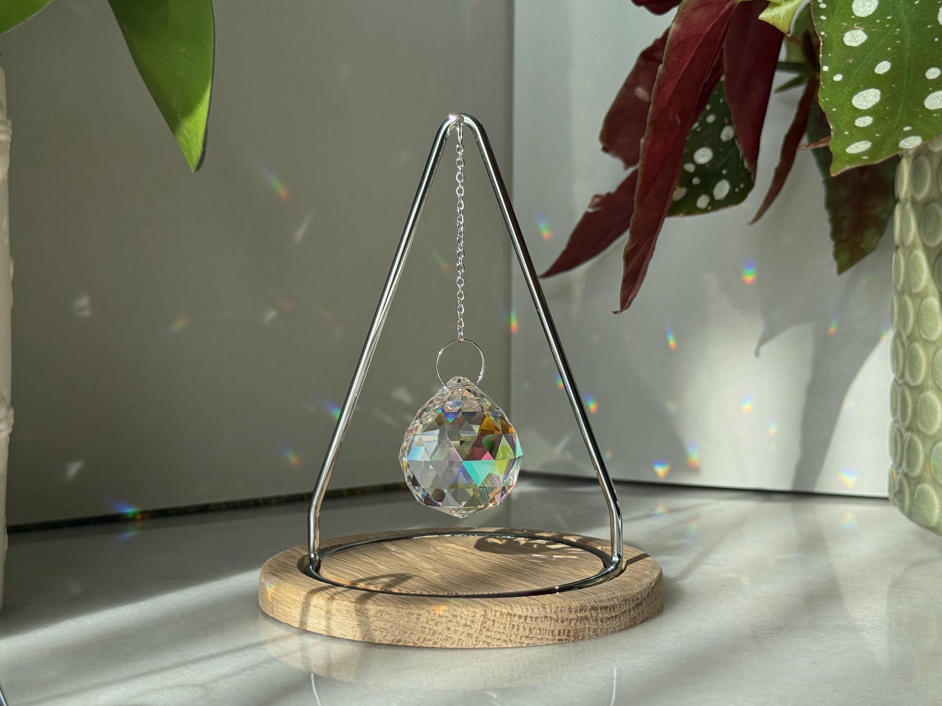 The Triangle Sonnenfänger: A modern crystal prism suncatcher with a handcrafted oak wood base and stainless steel frame, creating magical rainbow reflections.