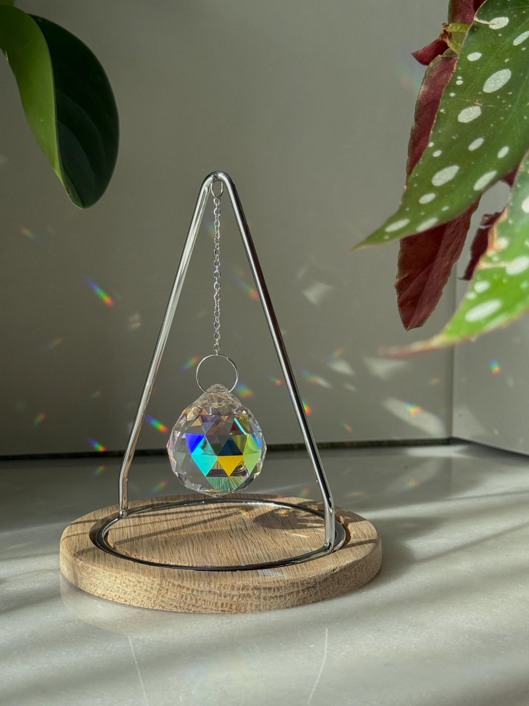The Triangle Sonnenfänger: A modern crystal prism suncatcher with a handcrafted oak wood base and stainless steel frame, creating magical rainbow reflections.
