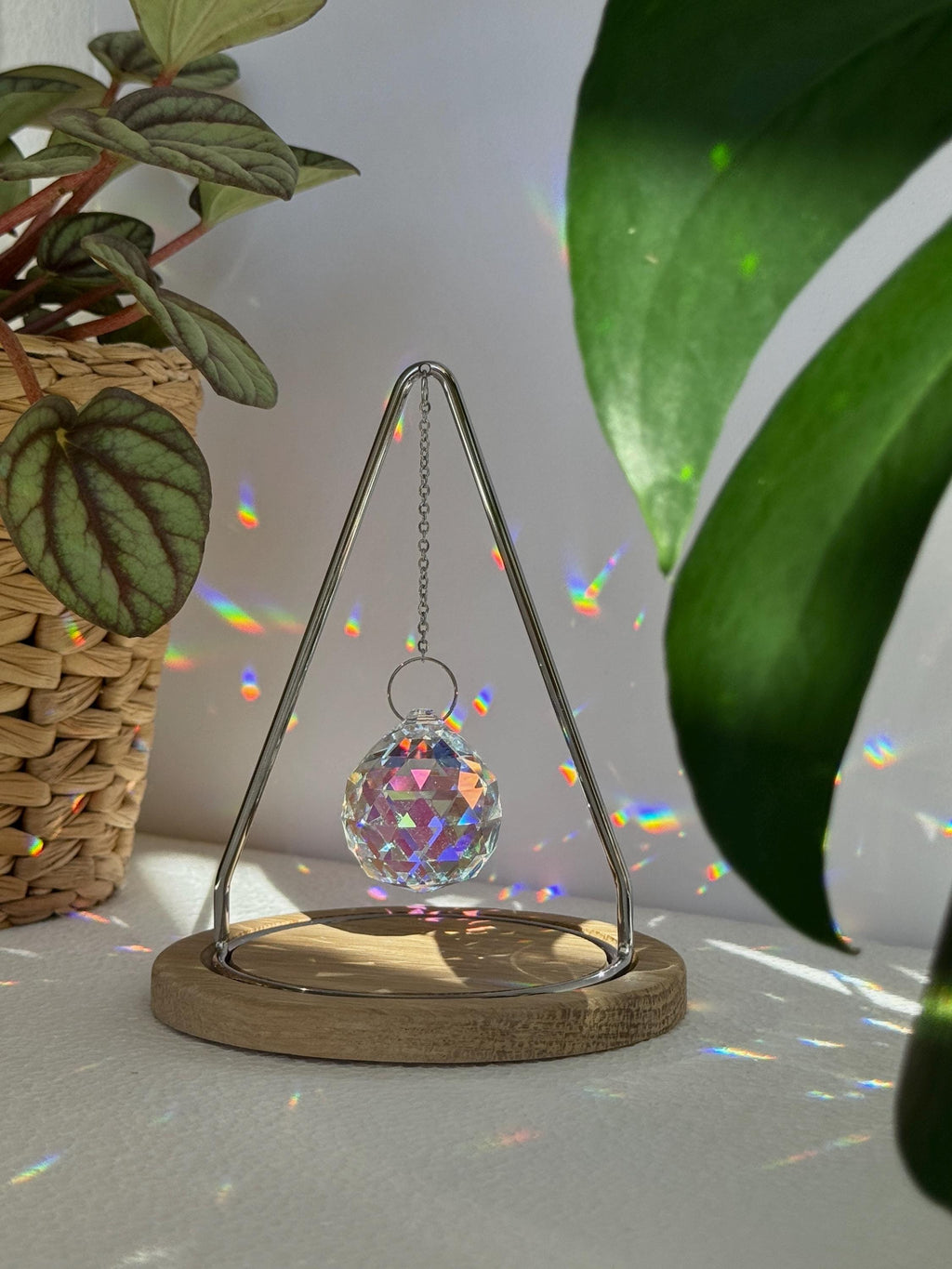 The Triangle Sonnenfänger: A modern crystal prism suncatcher with a handcrafted oak wood base and stainless steel frame, creating magical rainbow reflections.