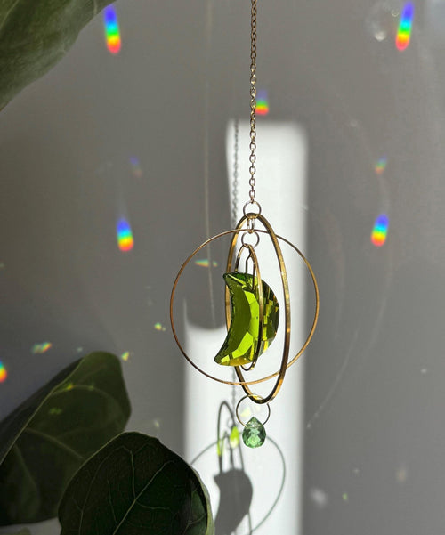 Handmade green crescent moon crystal suncatcher "Over the Moon" casting magical rainbows on a wall. Celestial gold ring window decor and rainbow maker (Sonnenfänger)
