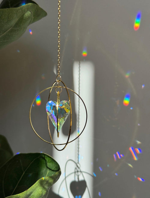 Handcrafted Sunkissed Heartbeat suncatcher with a faceted crystal heart and gold rings casting vibrant rainbows on a white wall.