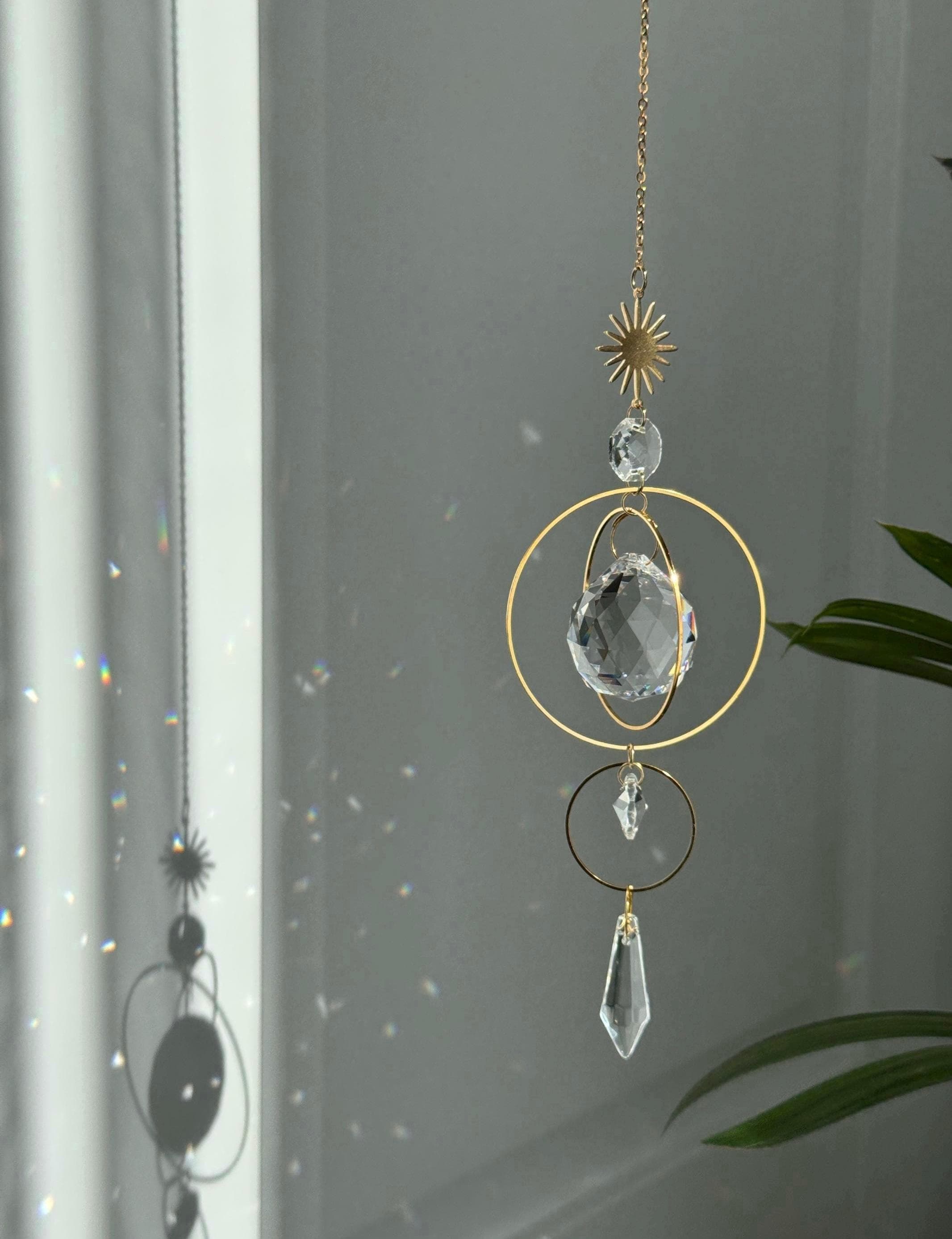 Gold celestial suncatcher with clear crystal prisms casting rainbow light reflections on a wall.