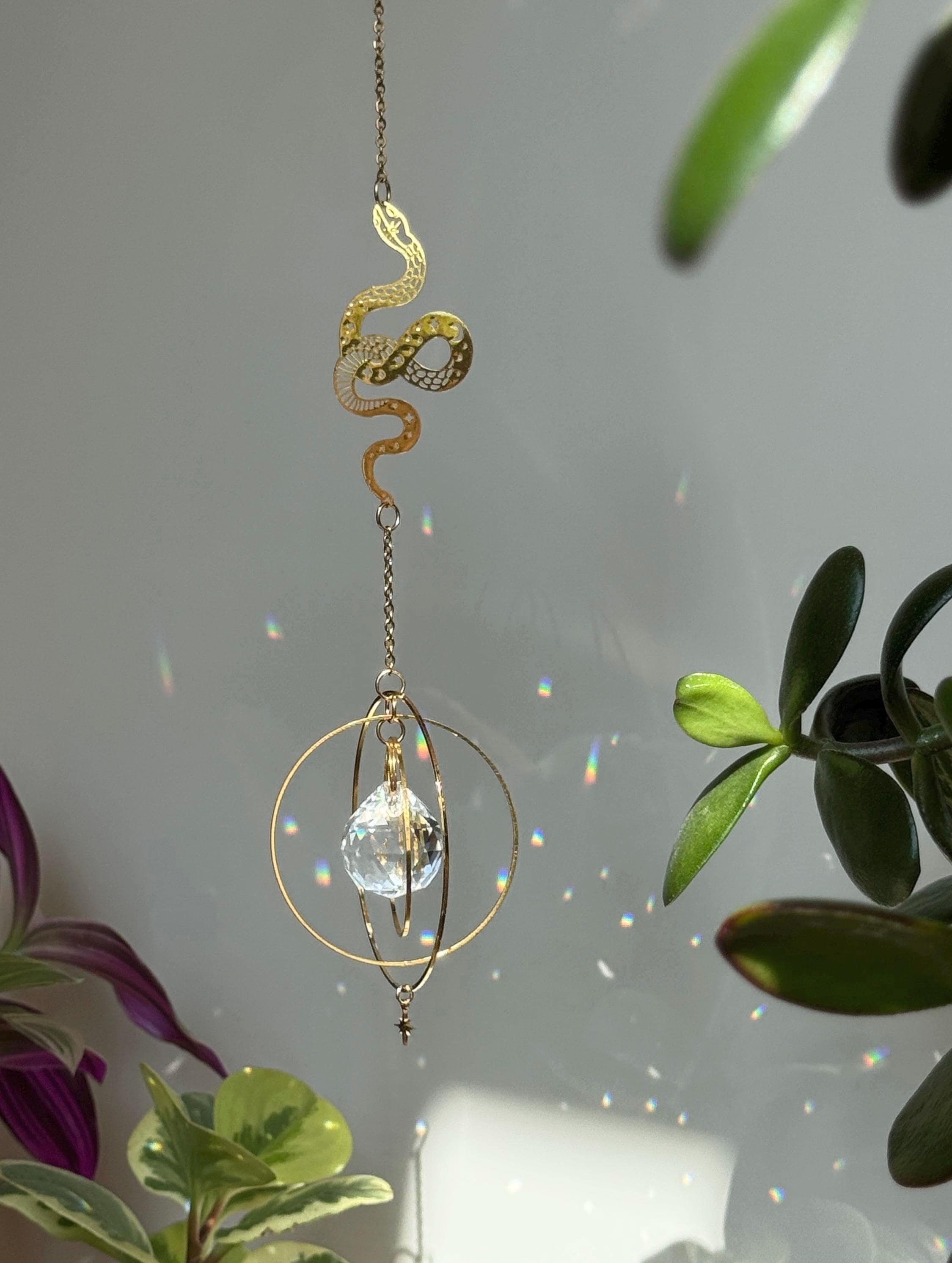 Decorative hanging crystal with gold chain against a blurred plant background