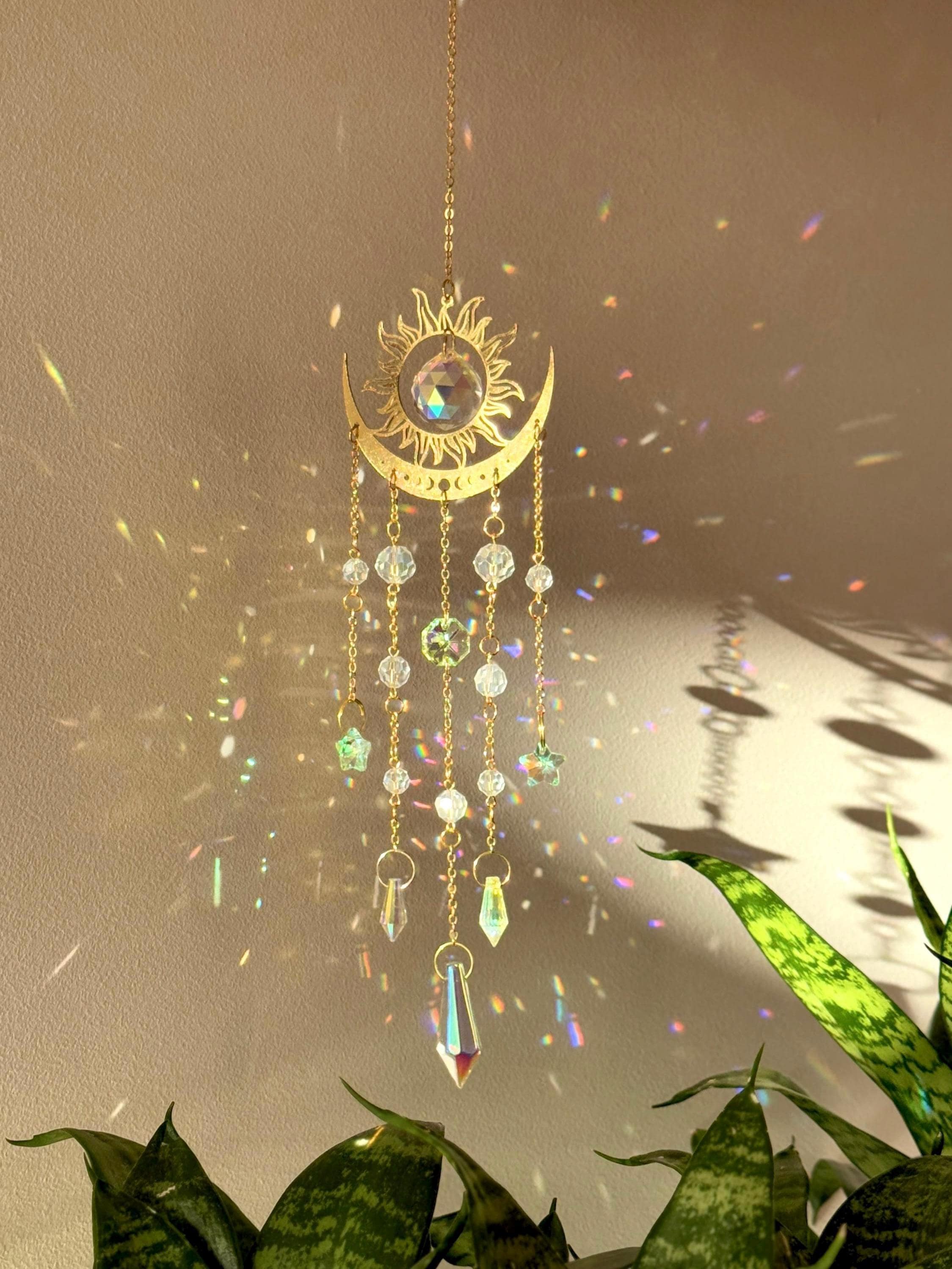 The Aura suncatcher featuring a gold crescent moon and sunburst with hanging crystal stars and prisms. Handgefertigter Sonnenfänger casting vivid rainbows on the wall. Boho-Stil Fensterdeko and magical Lichtreflexe home ornament.