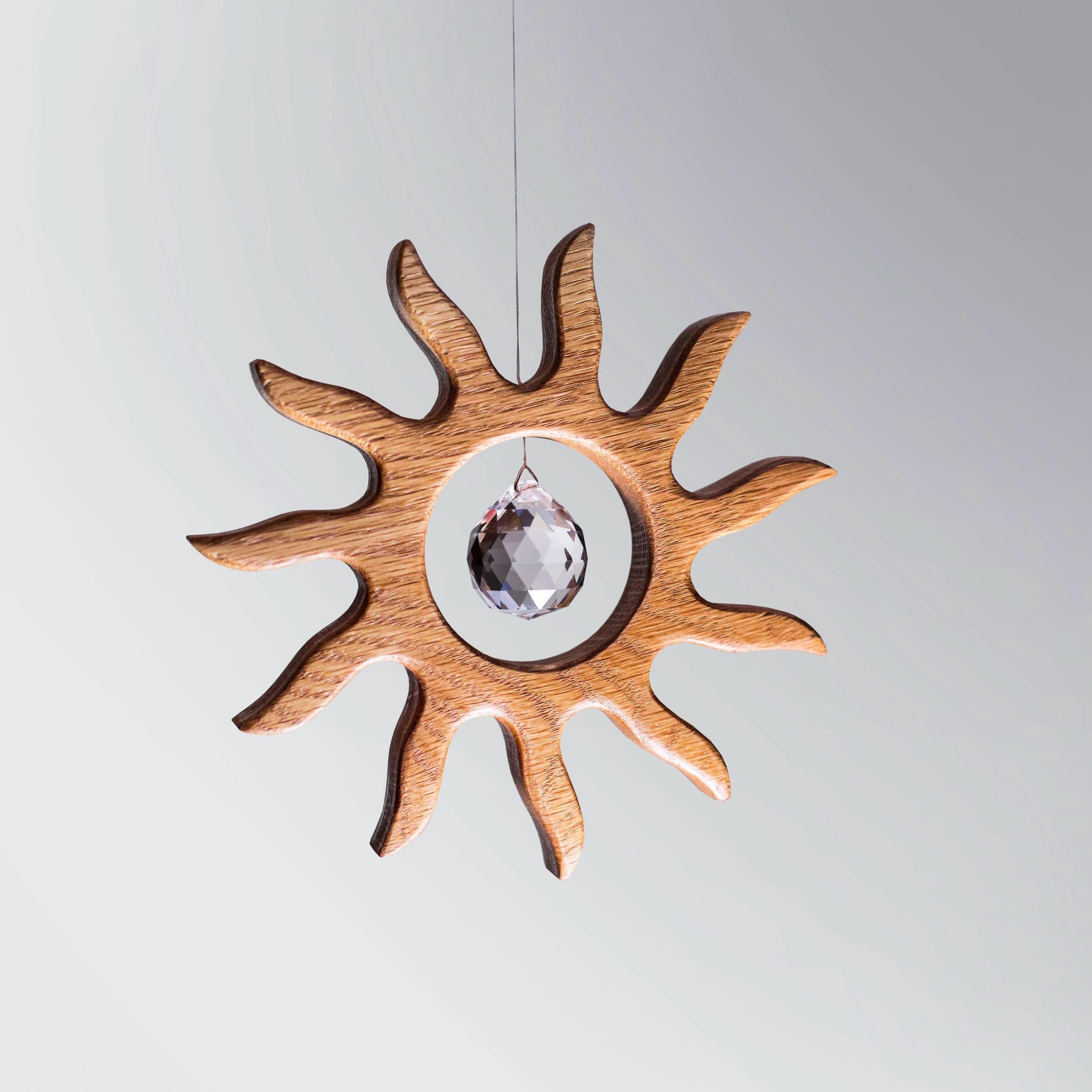 Handgefertigter Sonnenfänger aus Eichenholz (Oak) in Sonnenform with a central Asfour crystal prism. The Solstice wooden suncatcher casting rainbows on a white wall. Hochwertige Wohndekoration und Regenbogenmacher für Fenster oder Balkon.